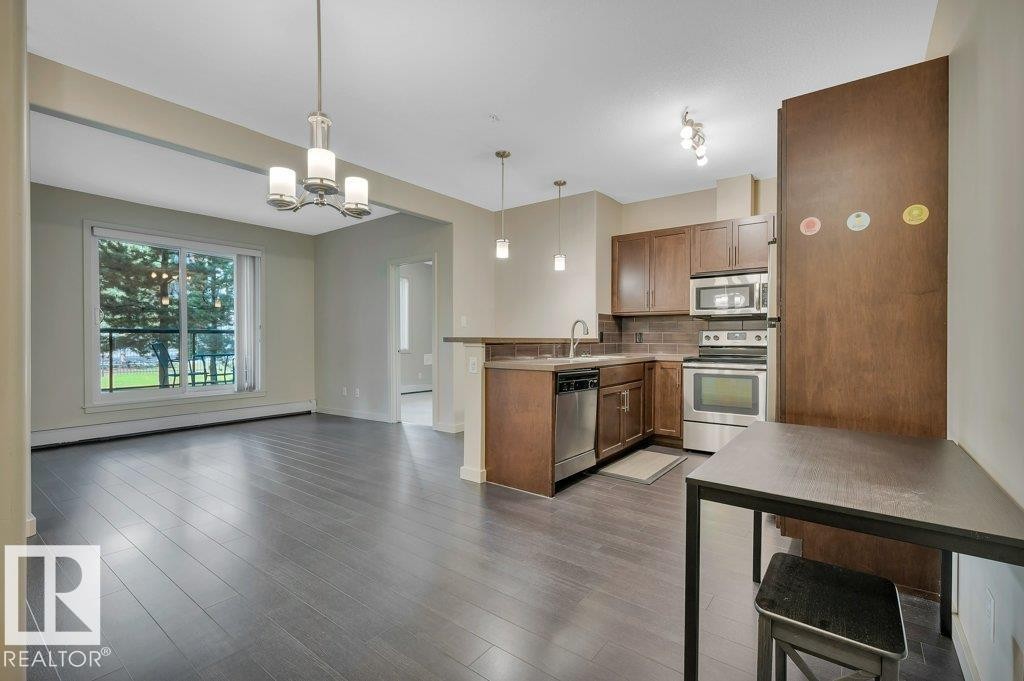 Kitchen with stainless steel appliances, backsplash, decorative light fixtures, a baseboard radiator, and a chandelier - 140 308 Ambleside Link, Edmonton, AB - Indoor Photo Showing Kitchen