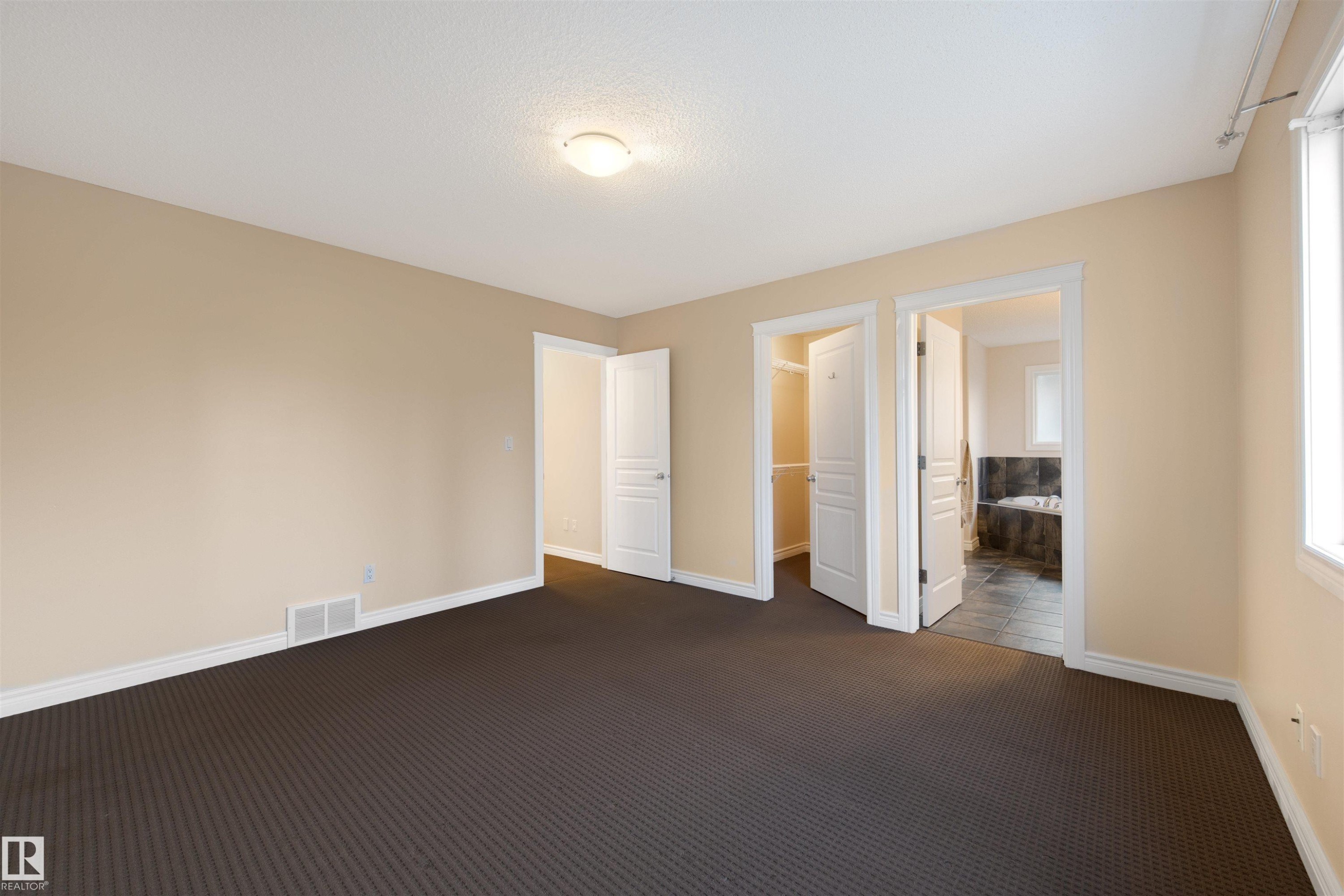 Unfurnished bedroom with a spacious closet, dark carpet, connected bathroom, and a textured ceiling - 2708 Miles Place, Edmonton, AB - Indoor Photo Showing Other Room
