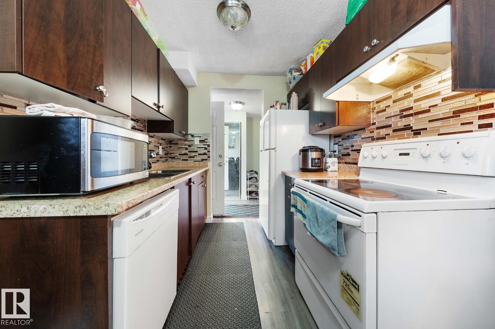Kitchen featuring white appliances, under cabinet range hood, light countertops, dark brown cabinets, and a textured ceiling - 285 Harrison Drive, Edmonton, AB - Indoor Photo Showing Kitchen