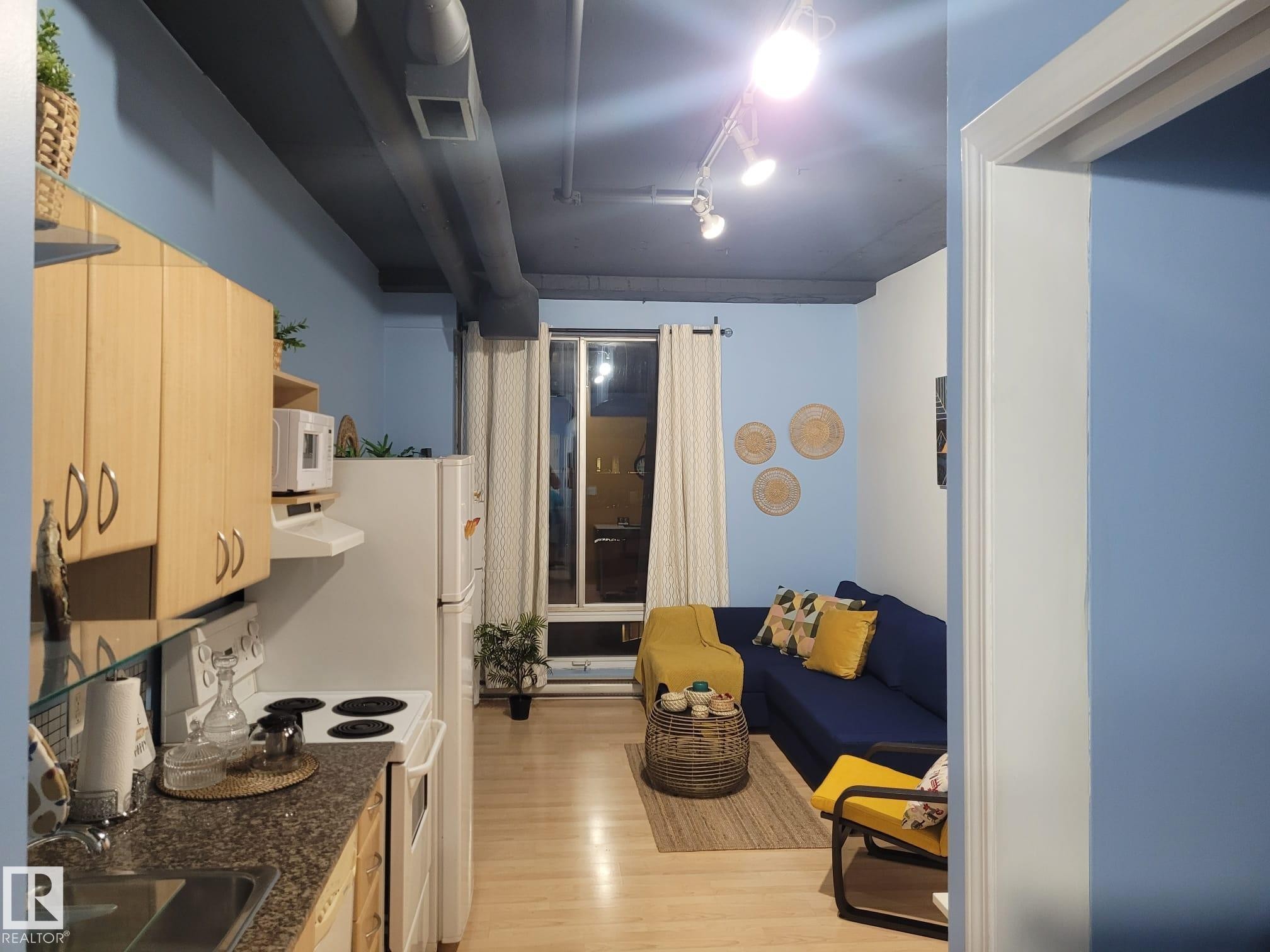 Kitchen featuring white appliances, light brown cabinetry, light wood-style floors, and extractor fan - 1704 10024 Jasper Avenue, Edmonton, AB - Indoor