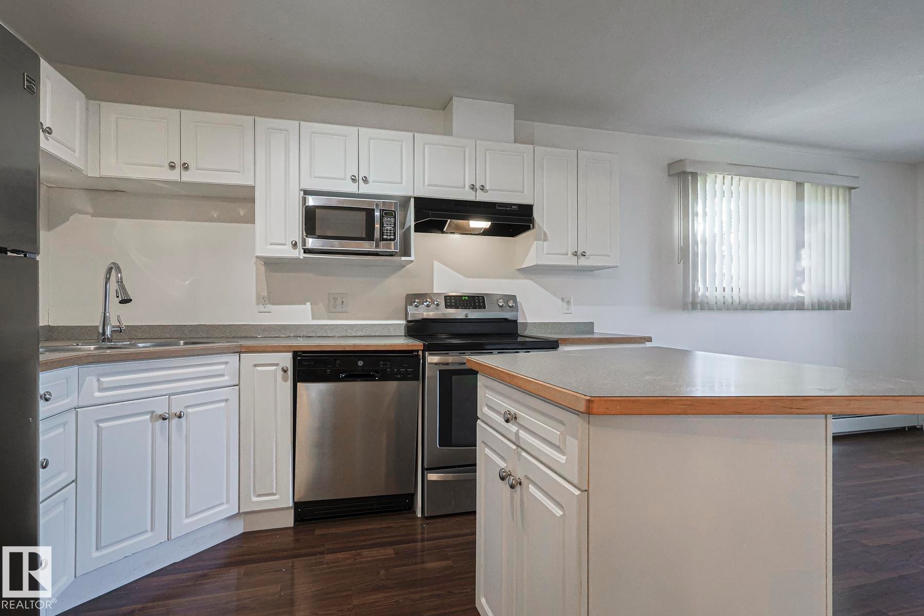 Kitchen featuring stainless steel appliances, dark wood-type flooring, and white cabinetry - 120 7511 171 Street Nw, Edmonton, AB - Indoor Photo Showing Kitchen