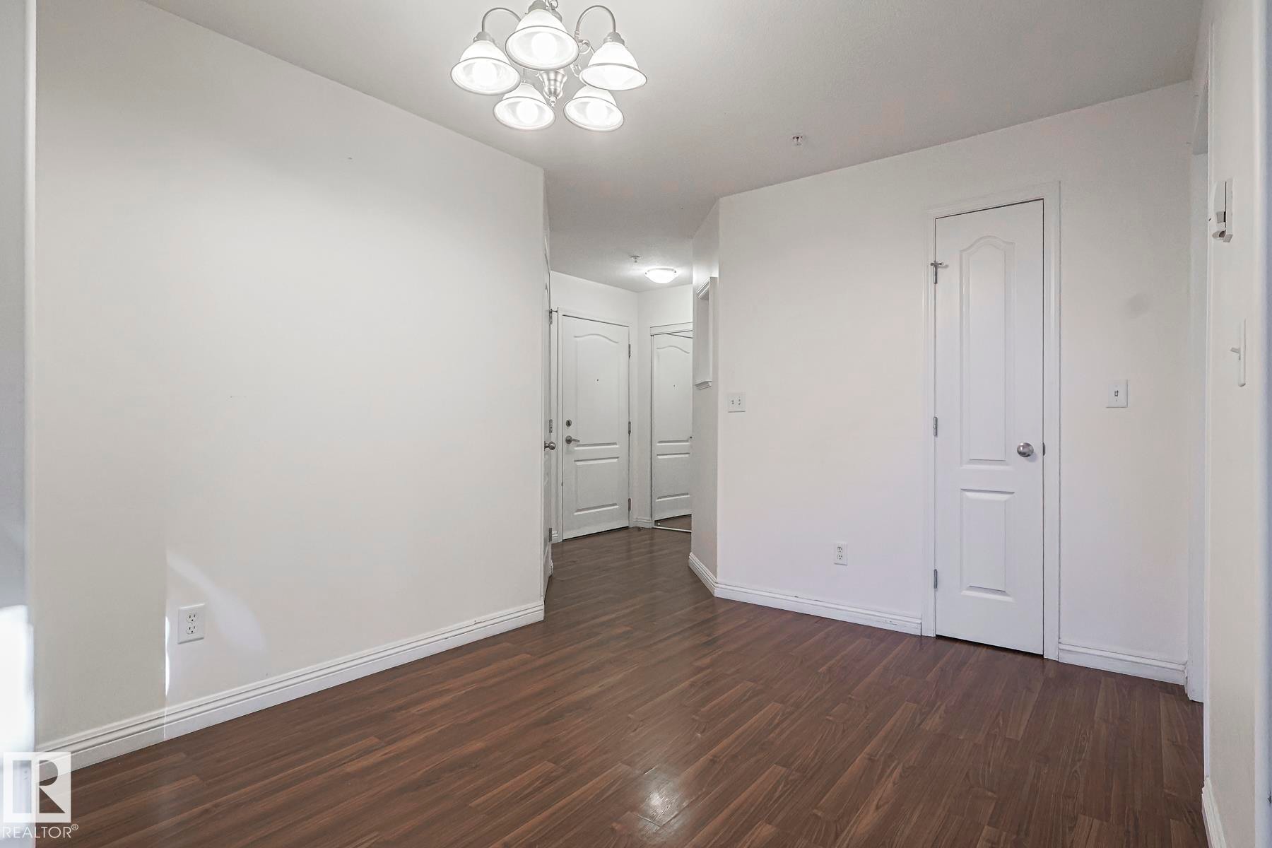 Empty room featuring dark wood finished floors and a chandelier - 120 7511 171 Street Nw, Edmonton, AB - Indoor Photo Showing Other Room