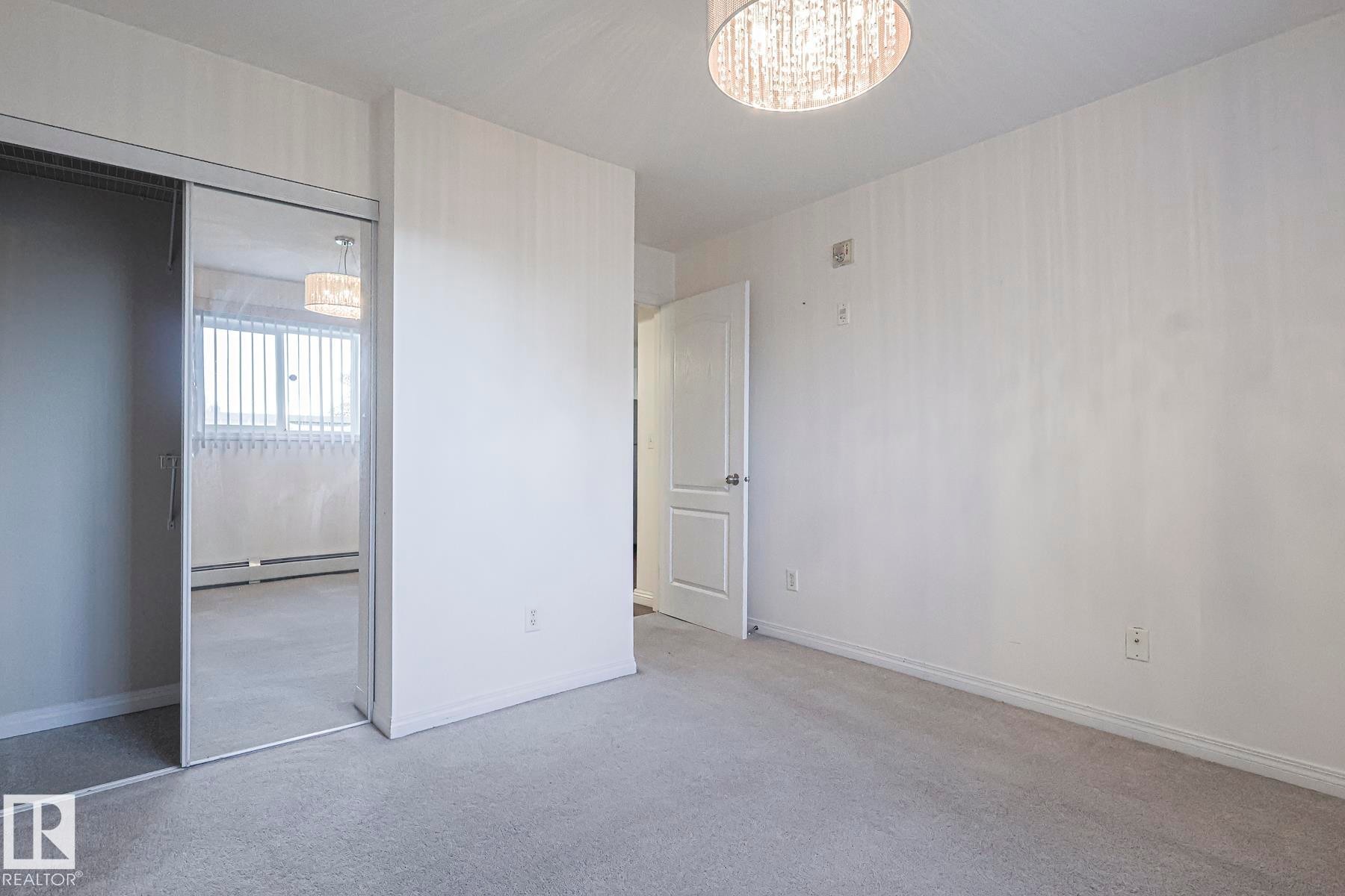 Unfurnished bedroom with light carpet, a closet, a baseboard heating unit, and a chandelier - 120 7511 171 Street Nw, Edmonton, AB - Indoor Photo Showing Other Room