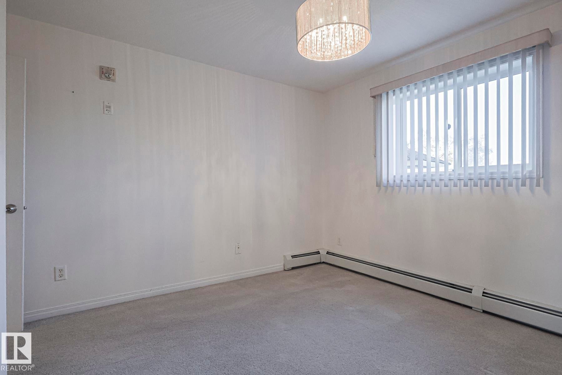 Unfurnished room with a baseboard heating unit, carpet floors, and a chandelier - 120 7511 171 Street Nw, Edmonton, AB - Indoor Photo Showing Other Room