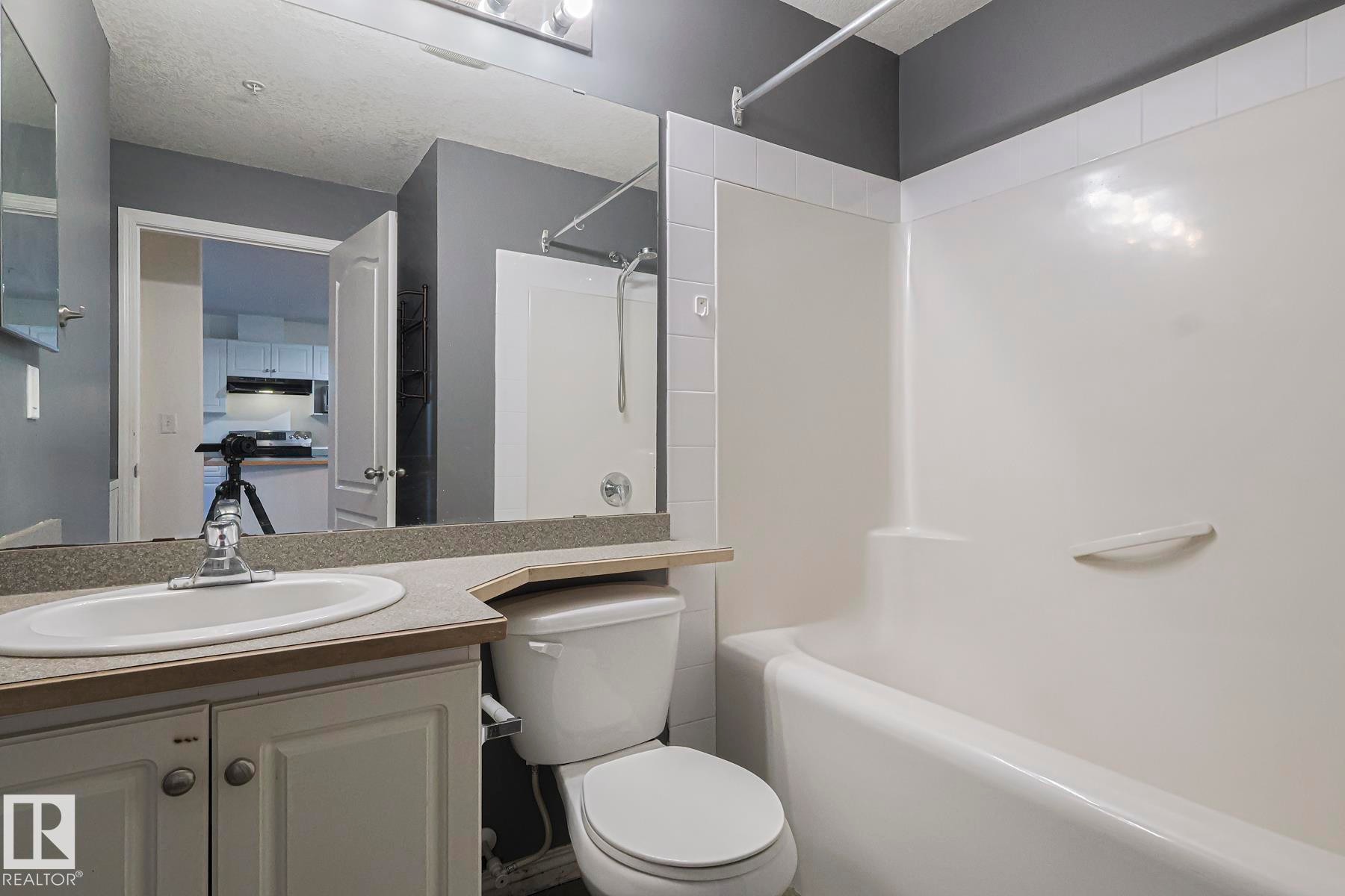 Full bathroom featuring vanity, washtub / shower combination, and a textured ceiling - 120 7511 171 Street Nw, Edmonton, AB - Indoor Photo Showing Bathroom