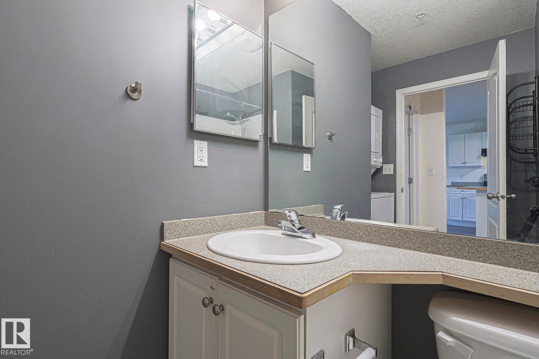 Bathroom with vanity, a textured ceiling, and washer / clothes dryer - 120 7511 171 Street Nw, Edmonton, AB - Indoor Photo Showing Bathroom