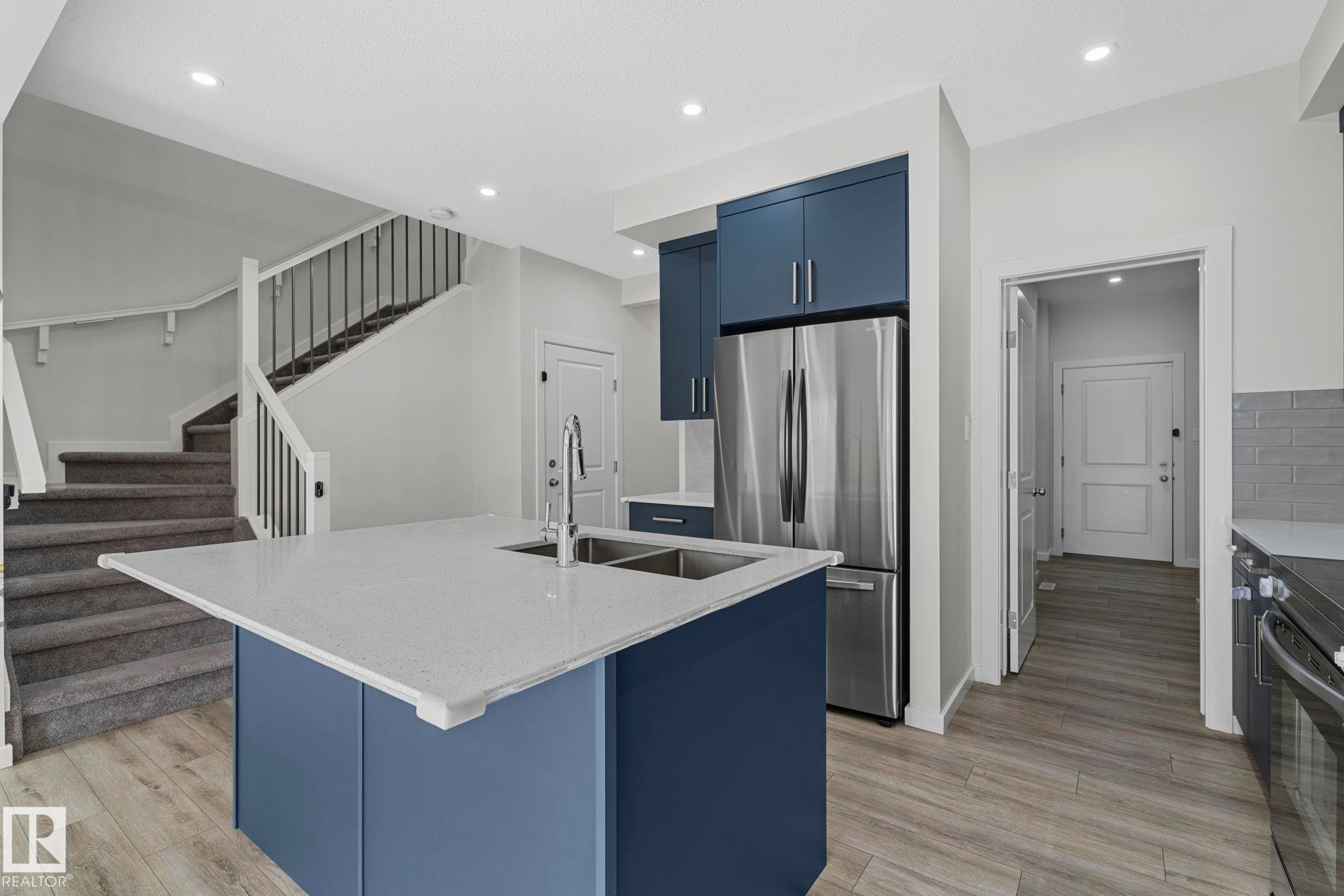 Kitchen featuring blue cabinetry, an island with sink, freestanding refrigerator, light stone counters, and recessed lighting - 1813 Collip View View, Edmonton, AB - Indoor Photo Showing Kitchen With Stainless Steel Kitchen With Double Sink With Upgraded Kitchen