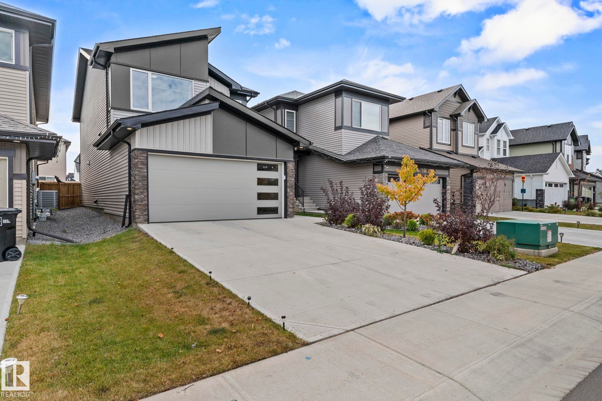 Modern home featuring stone siding, concrete driveway, an attached garage, and a residential view - 1813 Collip View View, Edmonton, AB - Outdoor