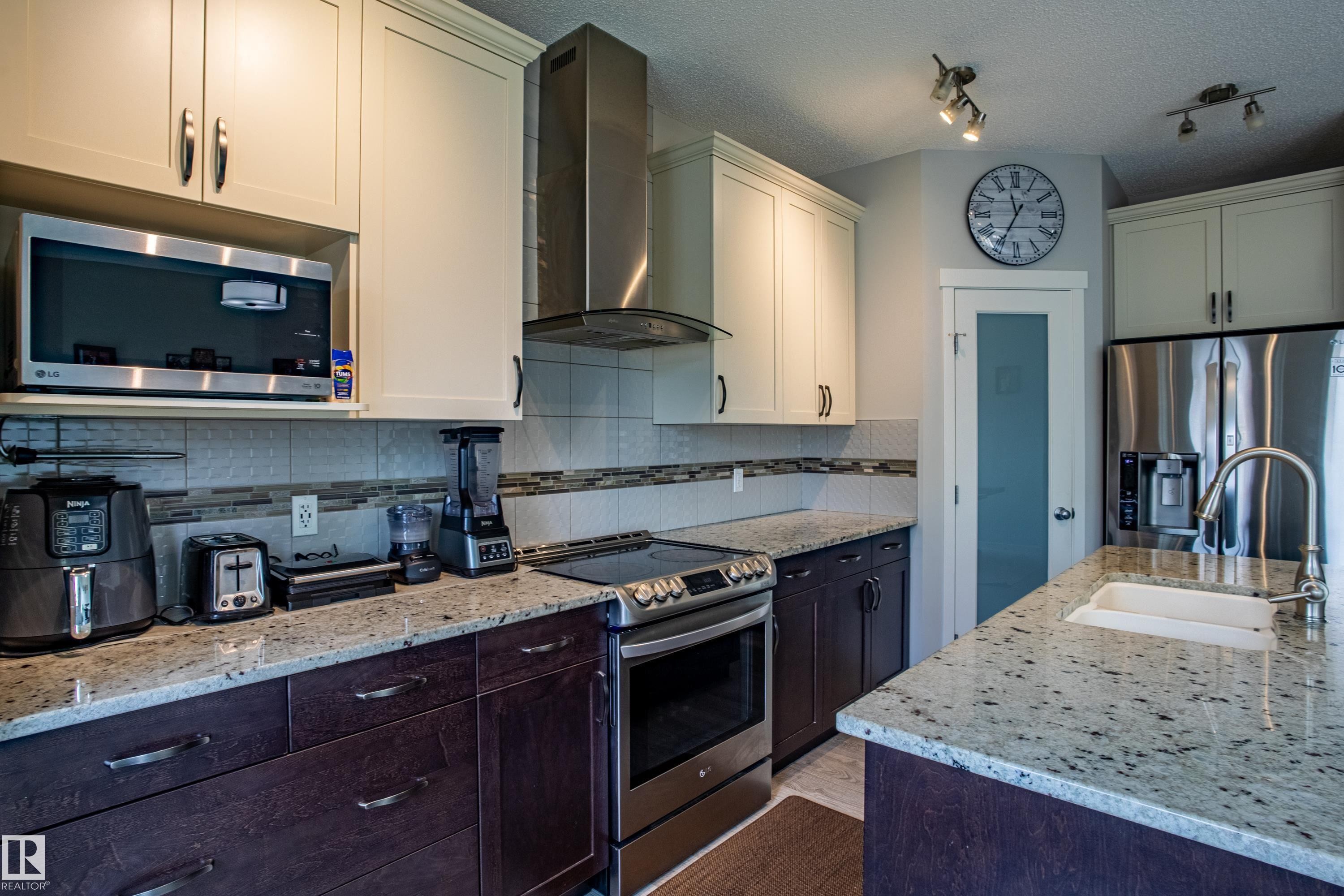 Kitchen with stainless steel appliances, wall chimney exhaust hood, light stone counters, backsplash, and a textured ceiling - 2407 Casey Link, Edmonton, AB - Indoor Photo Showing Kitchen With Upgraded Kitchen