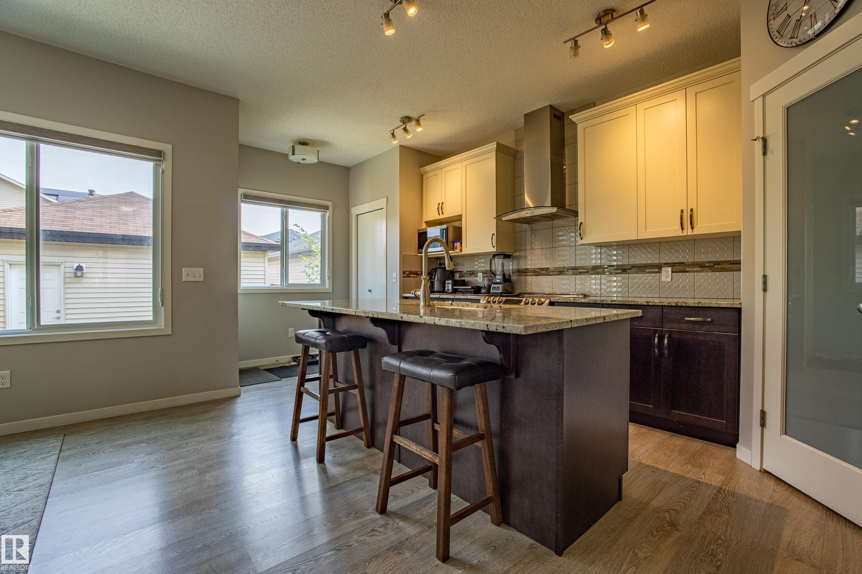 Kitchen featuring tasteful backsplash, dark brown cabinetry, a kitchen breakfast bar, a textured ceiling, and wall chimney exhaust hood - 2407 Casey Link, Edmonton, AB - Indoor Photo Showing Kitchen