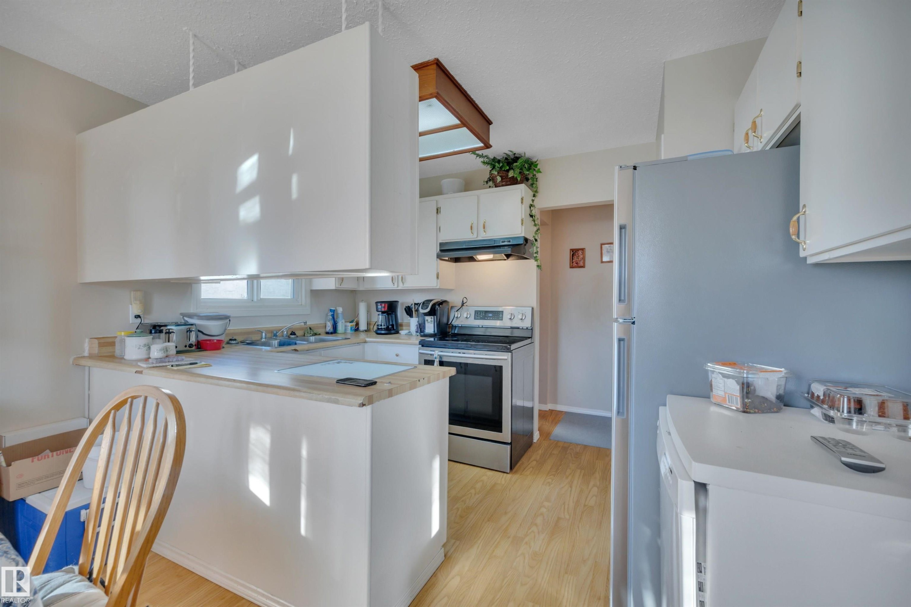 Kitchen with stainless steel range with electric cooktop, light countertops, a peninsula, white cabinets, and light wood finished floors - 5312 36 Ave, Wetaskiwin, AB - Indoor Photo Showing Kitchen