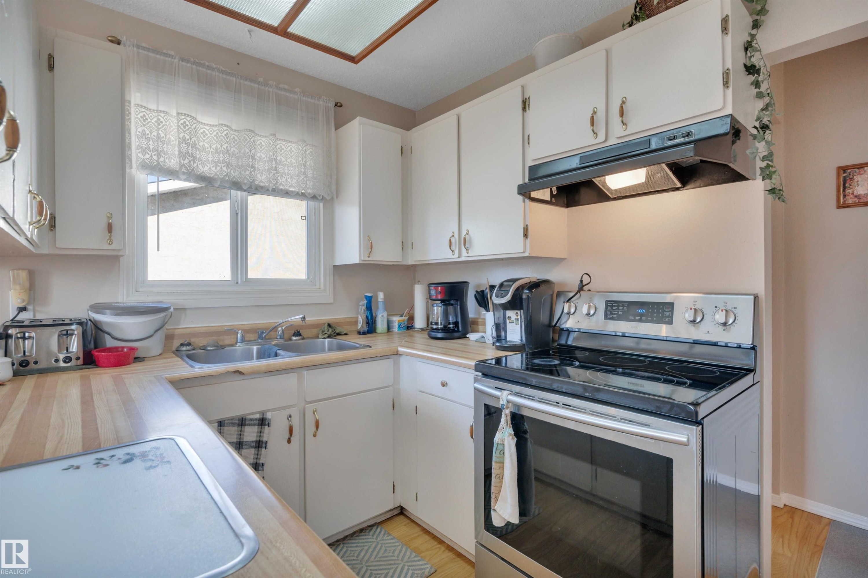 Kitchen featuring electric stove, light countertops, white cabinets, and under cabinet range hood - 5312 36 Ave, Wetaskiwin, AB - Indoor Photo Showing Kitchen With Double Sink