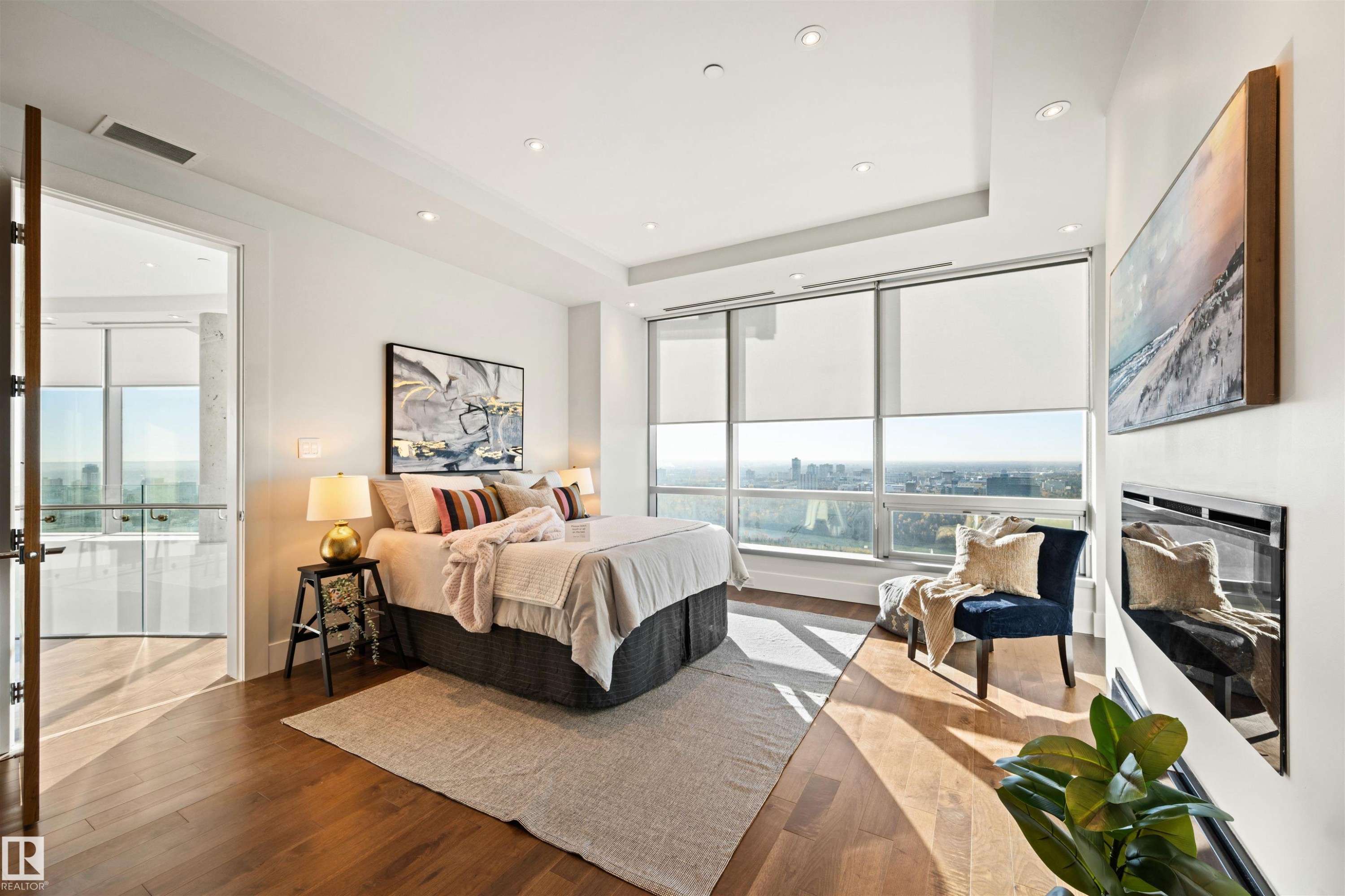 Bedroom with wood finished floors, a raised ceiling, recessed lighting, a glass covered fireplace, and a city view - 3201 11969 Jasper Avenue, Edmonton, AB - Indoor Photo Showing Bedroom