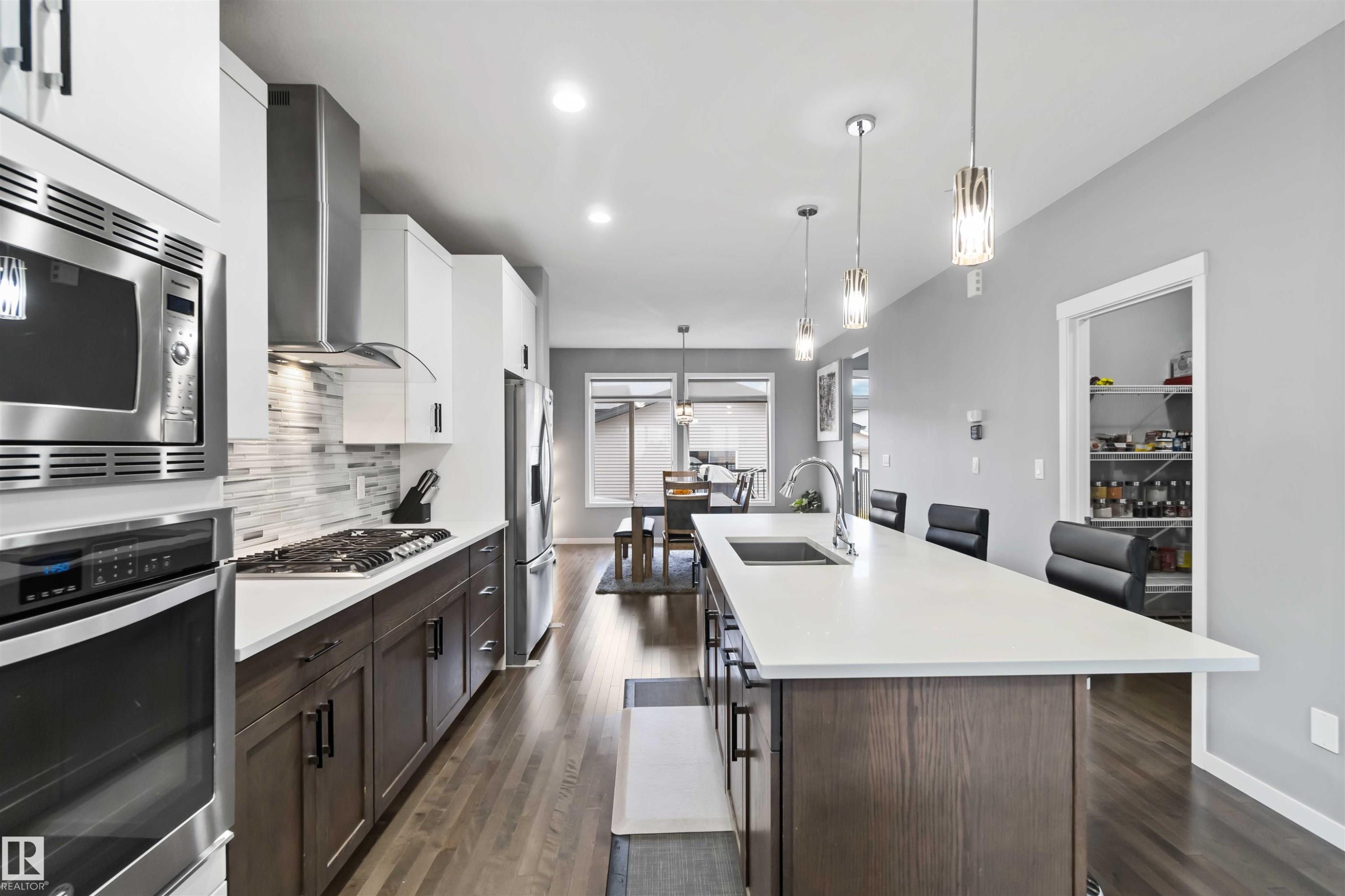 Kitchen featuring dark brown cabinets, stainless steel appliances, a large island, a kitchen bar, and recessed lighting - 17816 59 Street, Edmonton, AB
