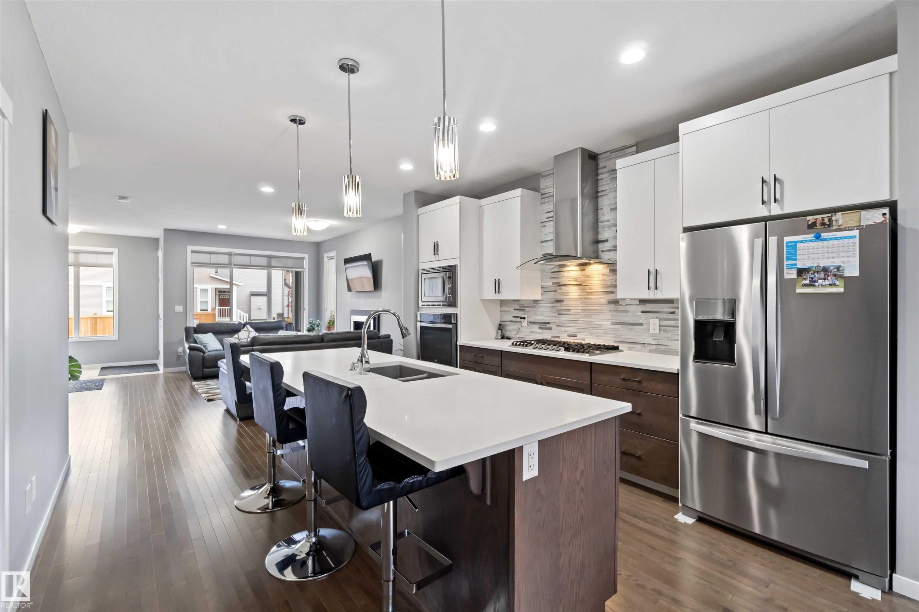 Kitchen with appliances with stainless steel finishes, backsplash, white cabinets, a breakfast bar, and an island with sink - 17816 59 Street, Edmonton, AB