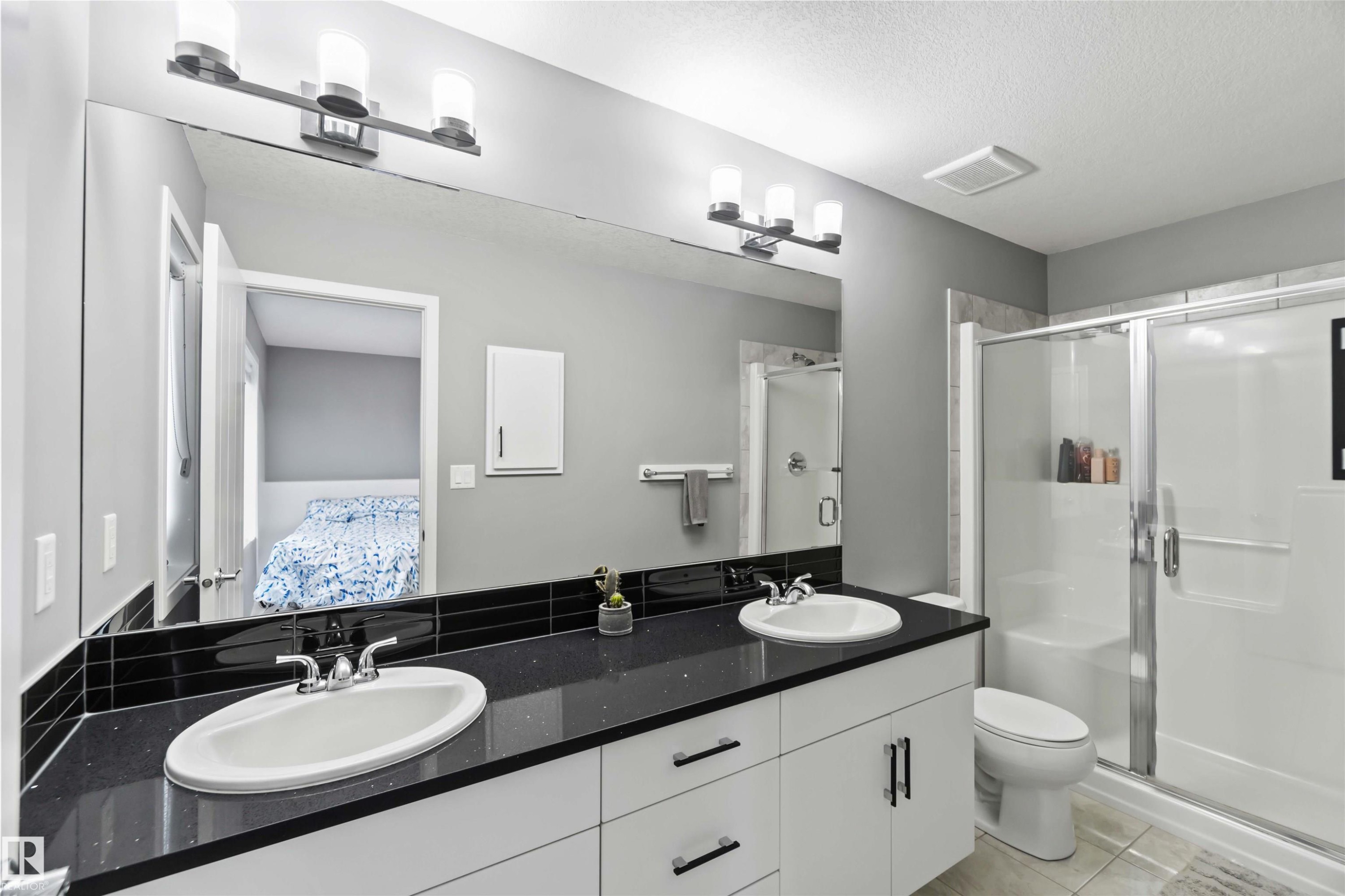 Full bathroom featuring double vanity, light tile patterned flooring, a stall shower, ensuite bath, and a textured ceiling - 17816 59 Street, Edmonton, AB