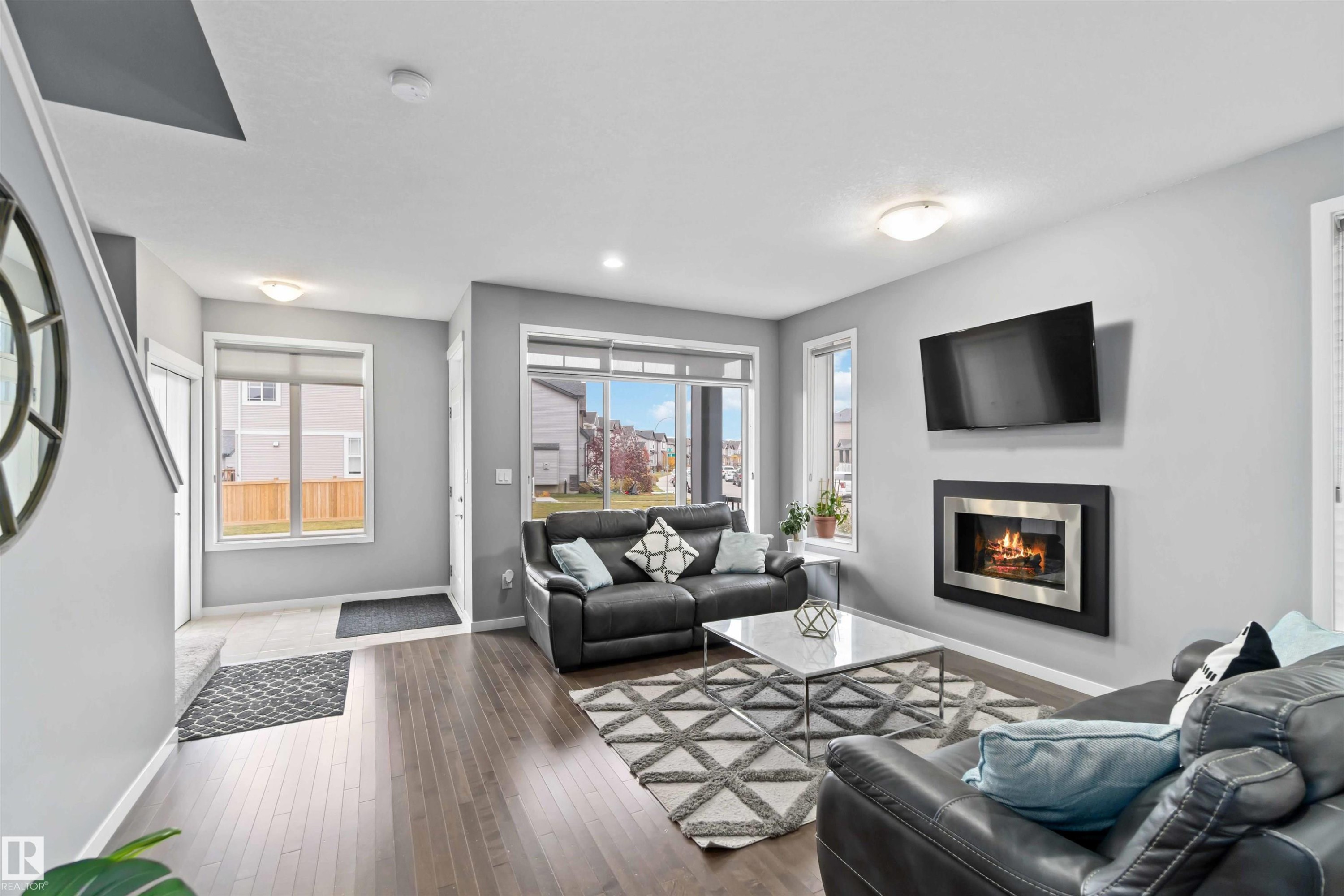 Living area with healthy amount of natural light, hardwood / wood-style floors, a glass covered fireplace, and stairs - 17816 59 Street, Edmonton, AB