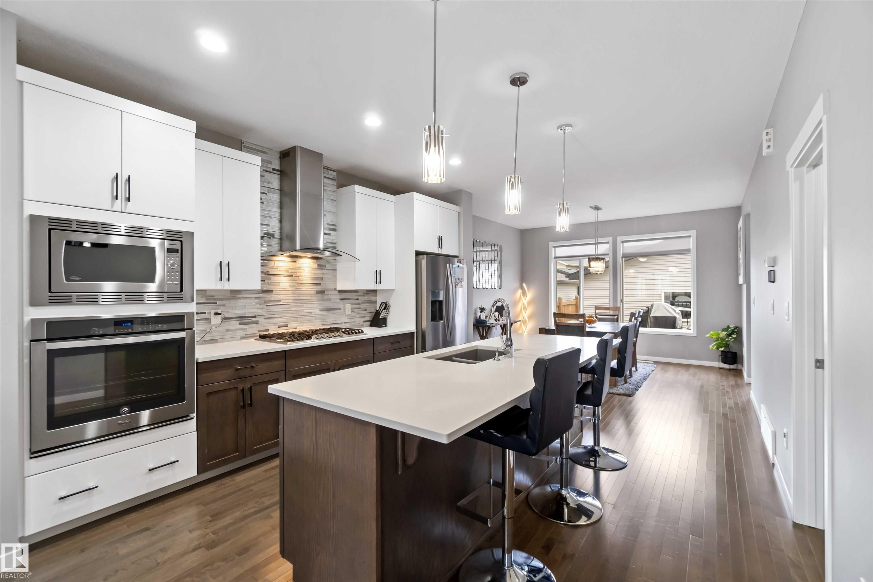 Kitchen with tasteful backsplash, a breakfast bar, appliances with stainless steel finishes, white cabinets, and dark brown cabinets - 17816 59 Street, Edmonton, AB
