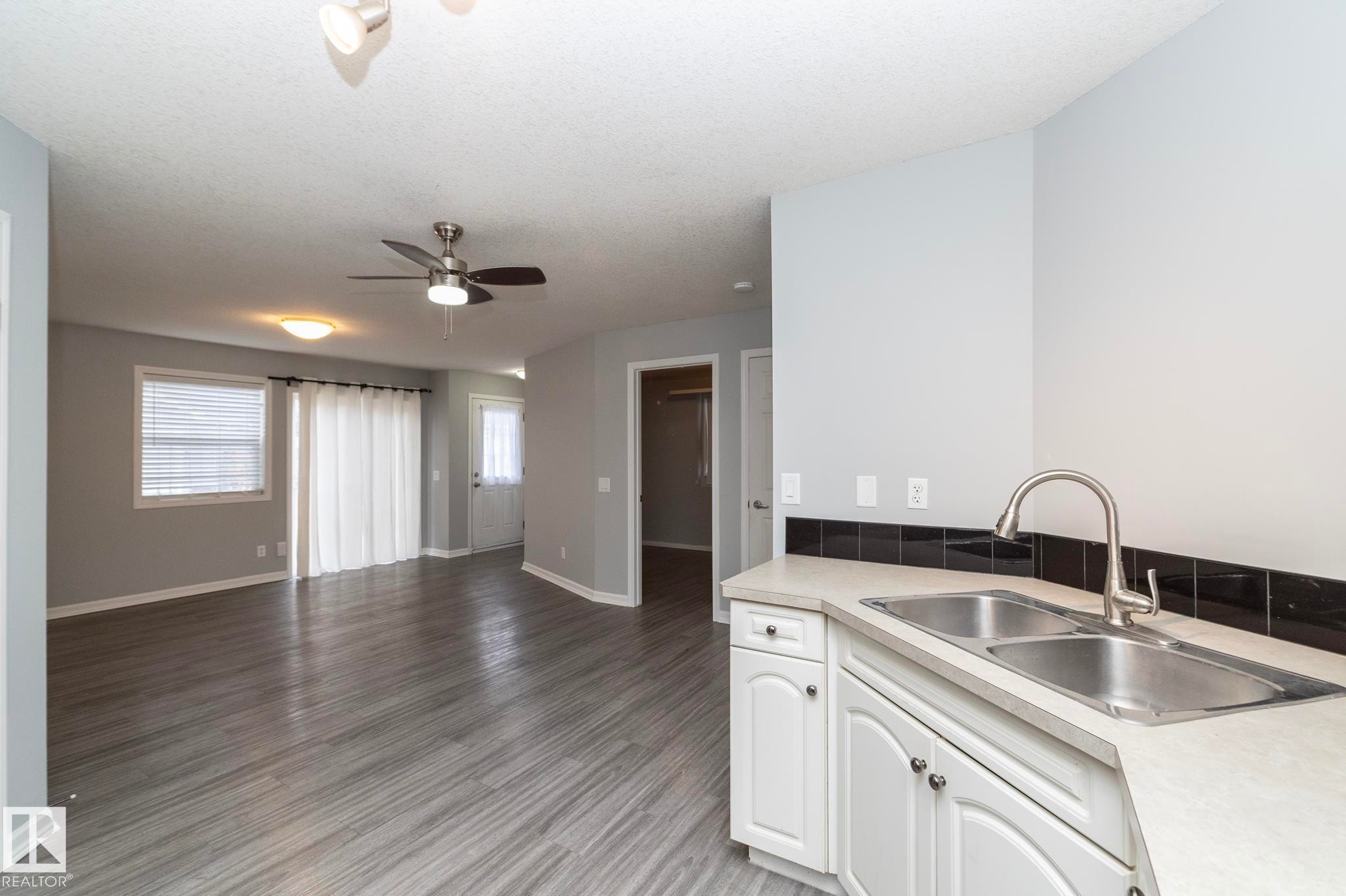 Kitchen with white cabinets, light wood finished floors, a textured ceiling, open floor plan, and ceiling fan - 1 150 Edwards Drive, Edmonton, AB - Indoor Photo Showing Kitchen With Double Sink