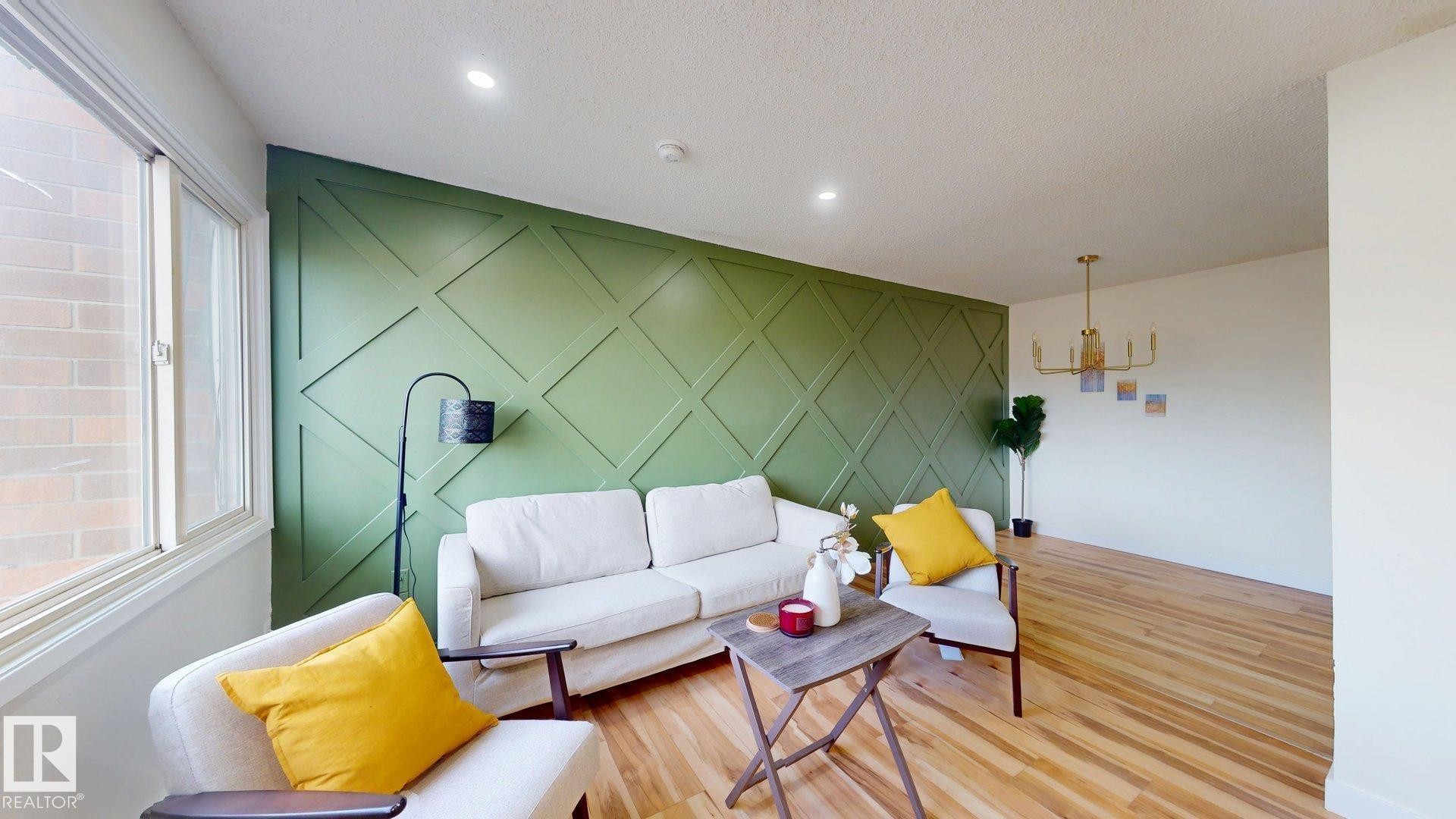 Living room featuring an accent wall, wood finished floors, a chandelier, and a textured ceiling - 114 2908 116A Avenue, Edmonton, AB - Indoor