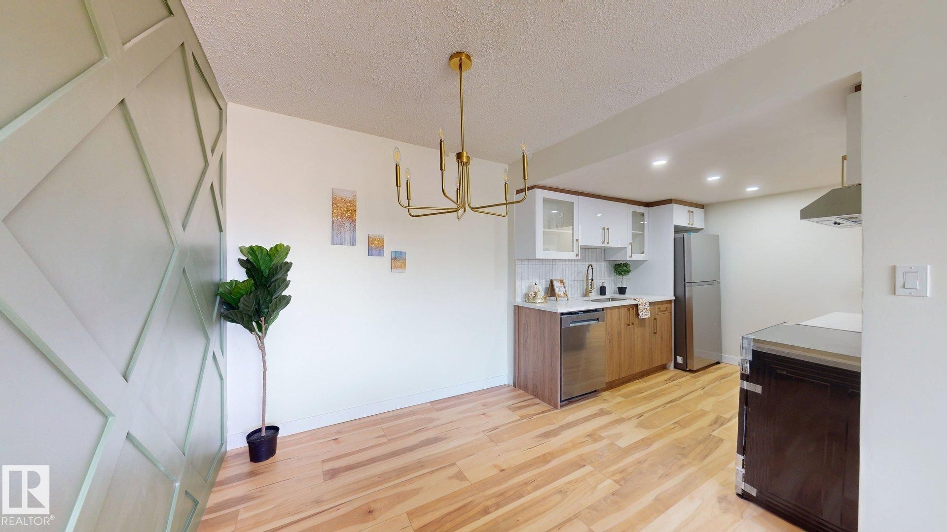 Kitchen featuring brown cabinets, light countertops, glass insert cabinets, light wood finished floors, and white cabinetry - 114 2908 116A Avenue, Edmonton, AB - Indoor
