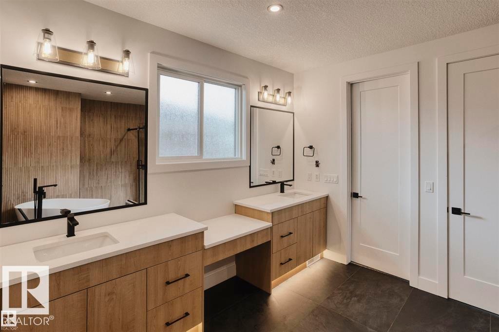 Bathroom with a textured ceiling, dark tile patterned flooring, two vanities, a freestanding tub, and recessed lighting - 63 Jubilation Drive, St. Albert, AB - Indoor