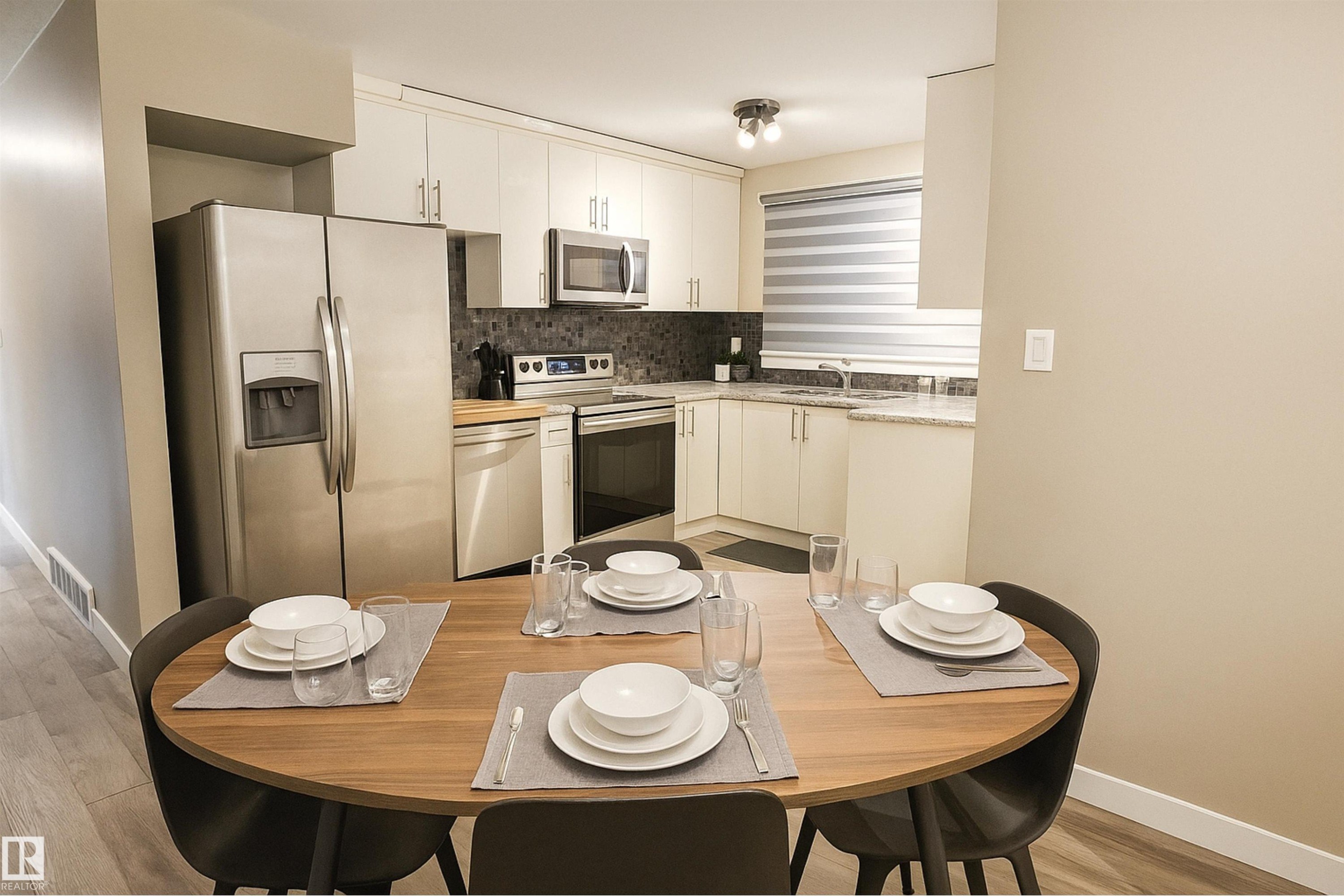 Kitchen with appliances with stainless steel finishes, decorative backsplash, white cabinetry, and light wood-type flooring - 4203 83 Street, Edmonton, AB - Indoor