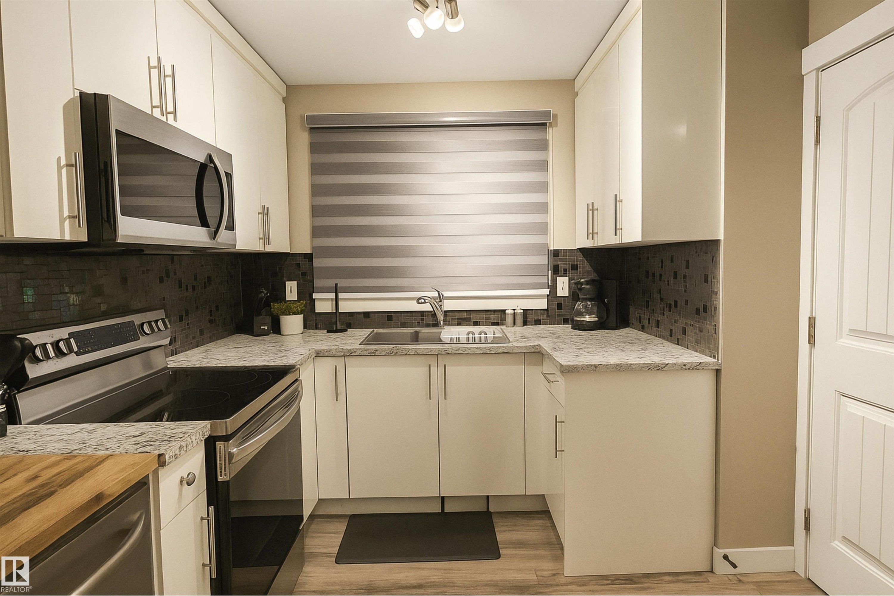 Kitchen with decorative backsplash, stainless steel appliances, white cabinetry, light wood finished floors, and light stone counters - 4203 83 Street, Edmonton, AB - Indoor Photo Showing Kitchen