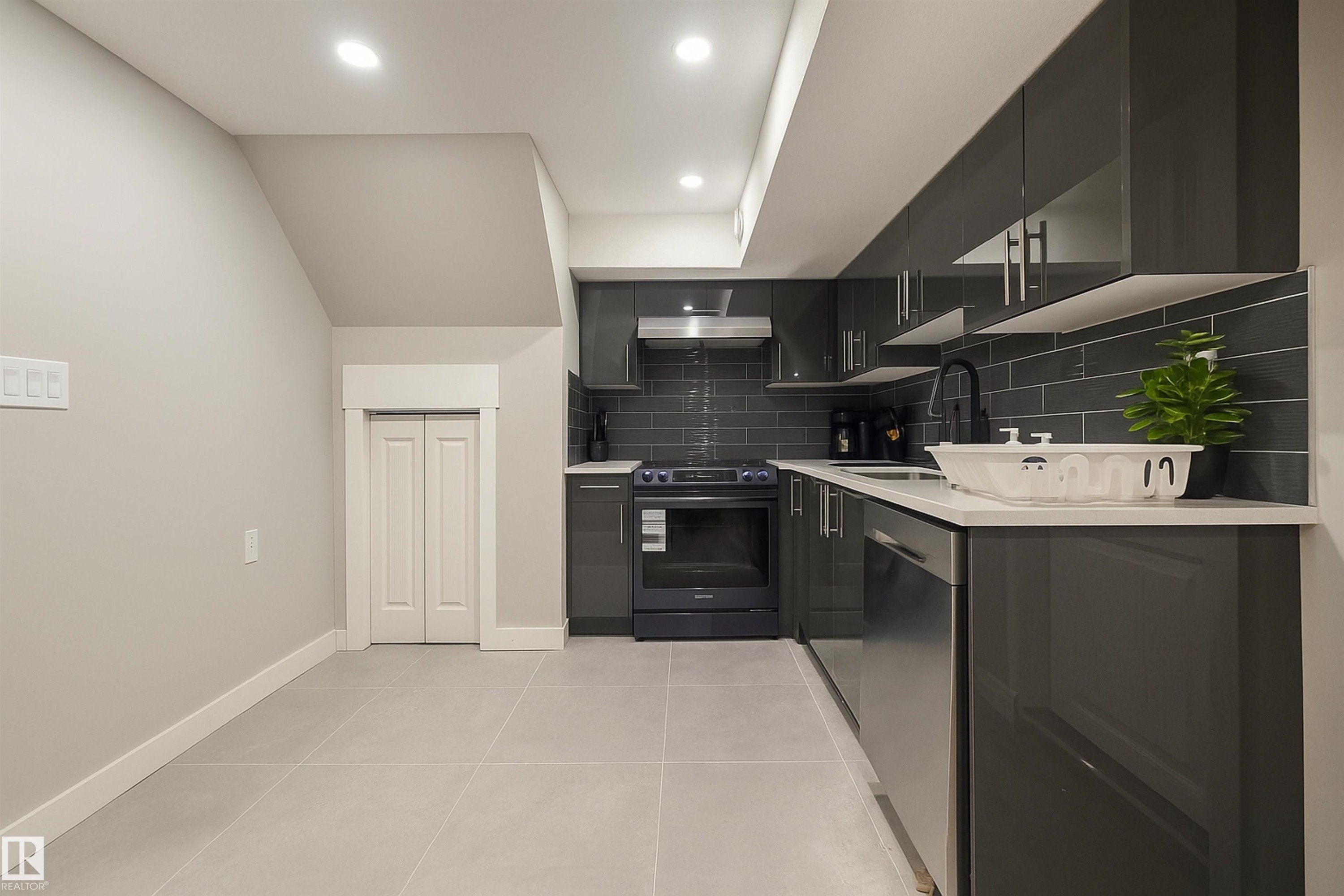 Kitchen featuring dark cabinetry, backsplash, black electric range oven, light tile patterned floors, and stainless steel dishwasher - 4203 83 Street, Edmonton, AB - Indoor Photo Showing Kitchen