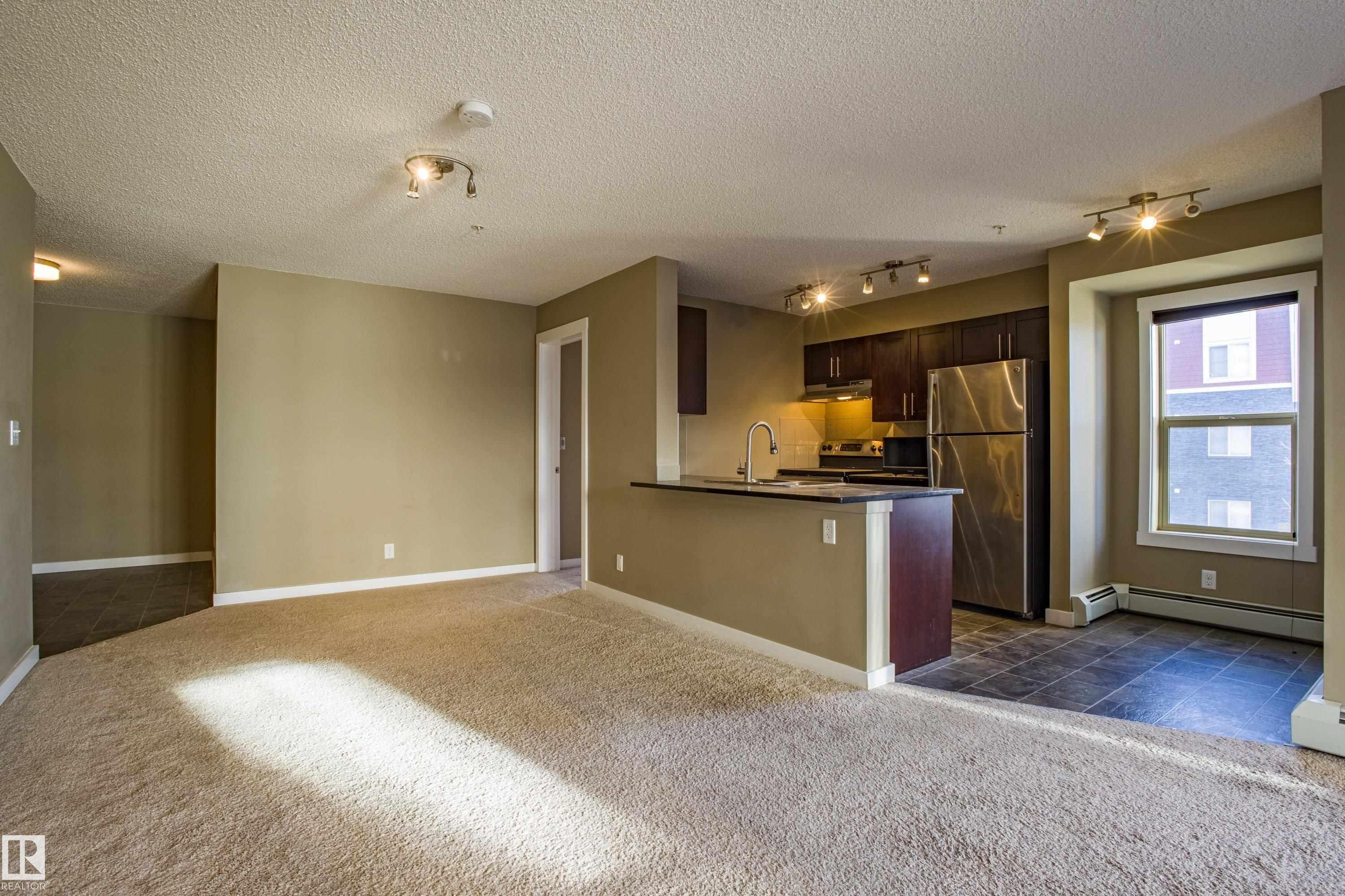 Kitchen with dark brown cabinetry, appliances with stainless steel finishes, open floor plan, dark colored carpet, and dark countertops - 201 5804 Mullen Place, Edmonton, AB - Indoor Photo Showing Kitchen