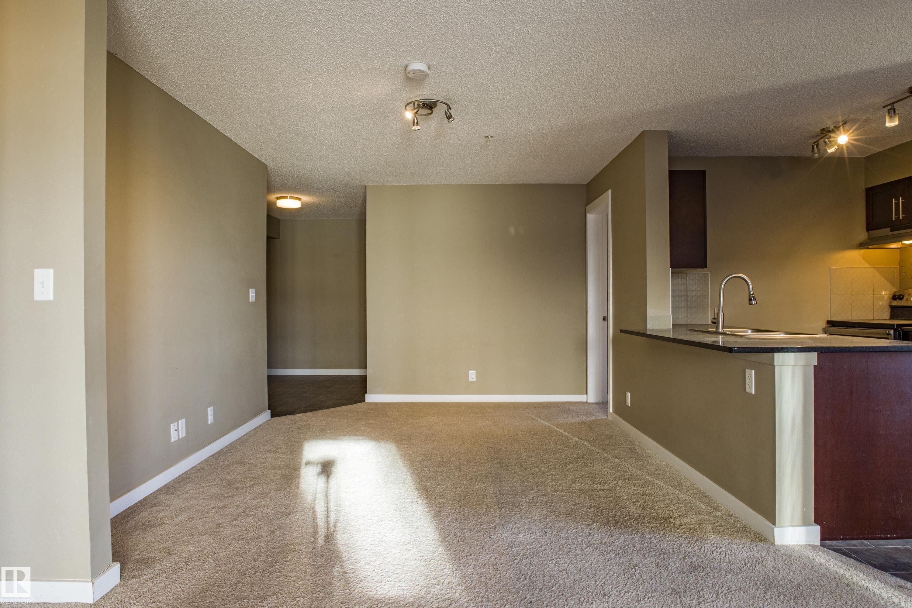 Unfurnished dining area featuring a textured ceiling and light colored carpet - 201 5804 Mullen Place, Edmonton, AB - Indoor Photo Showing Kitchen