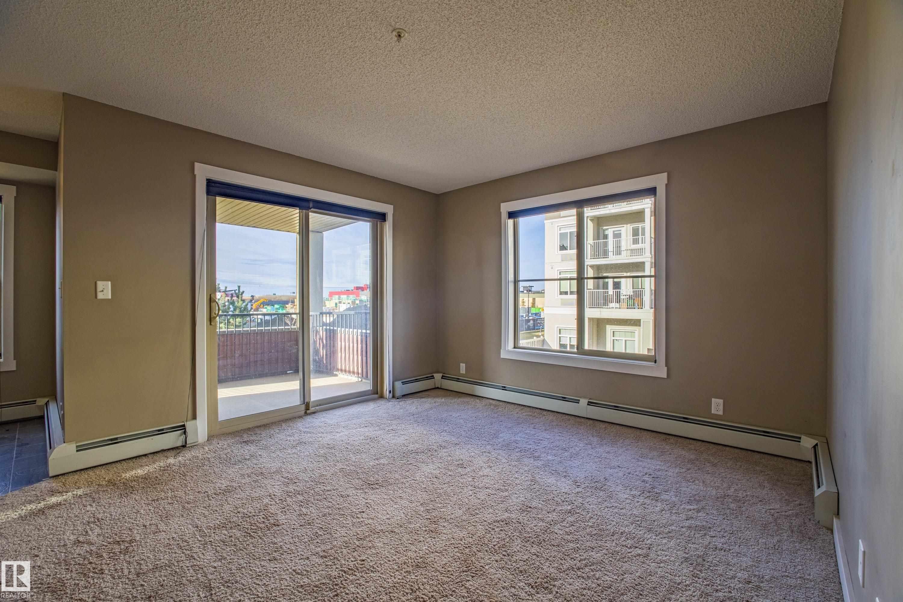 Empty room with a textured ceiling, carpet floors, and baseboard heating - 201 5804 Mullen Place, Edmonton, AB - Indoor Photo Showing Other Room