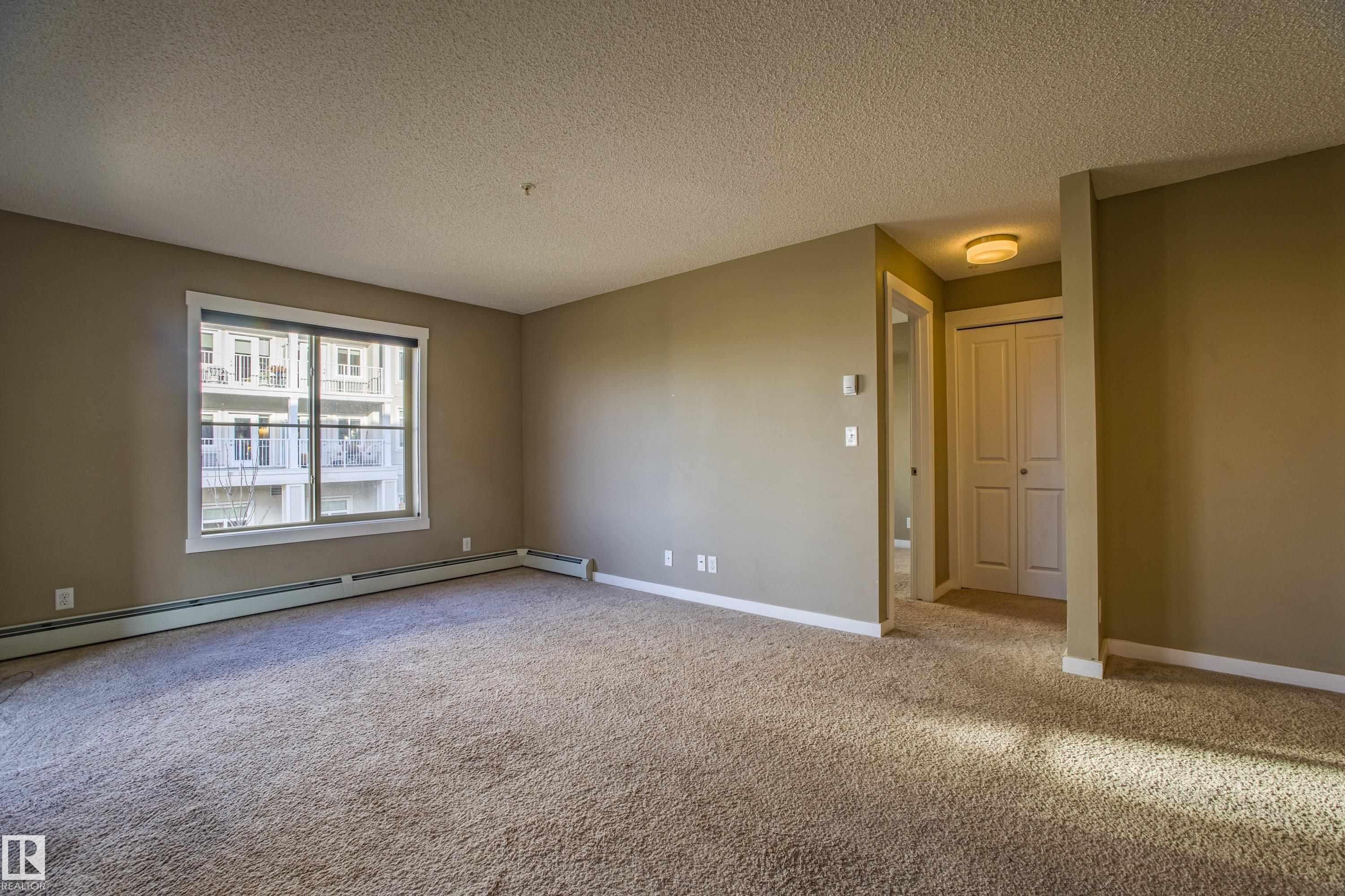 Carpeted empty room featuring a textured ceiling and a baseboard radiator - 201 5804 Mullen Place, Edmonton, AB - Indoor Photo Showing Other Room