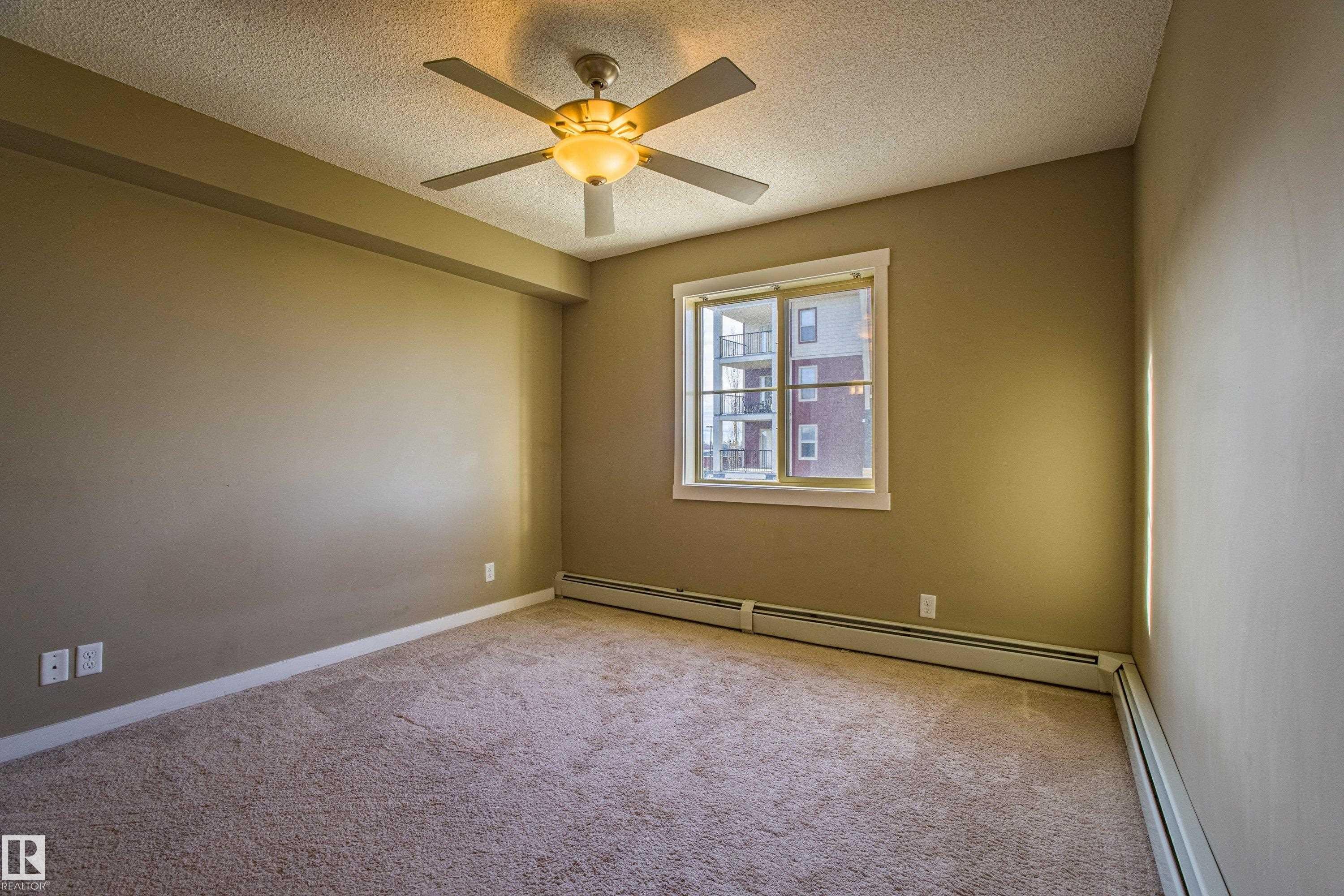 Carpeted spare room with a baseboard radiator, a textured ceiling, and a ceiling fan - 201 5804 Mullen Place, Edmonton, AB - Indoor Photo Showing Other Room