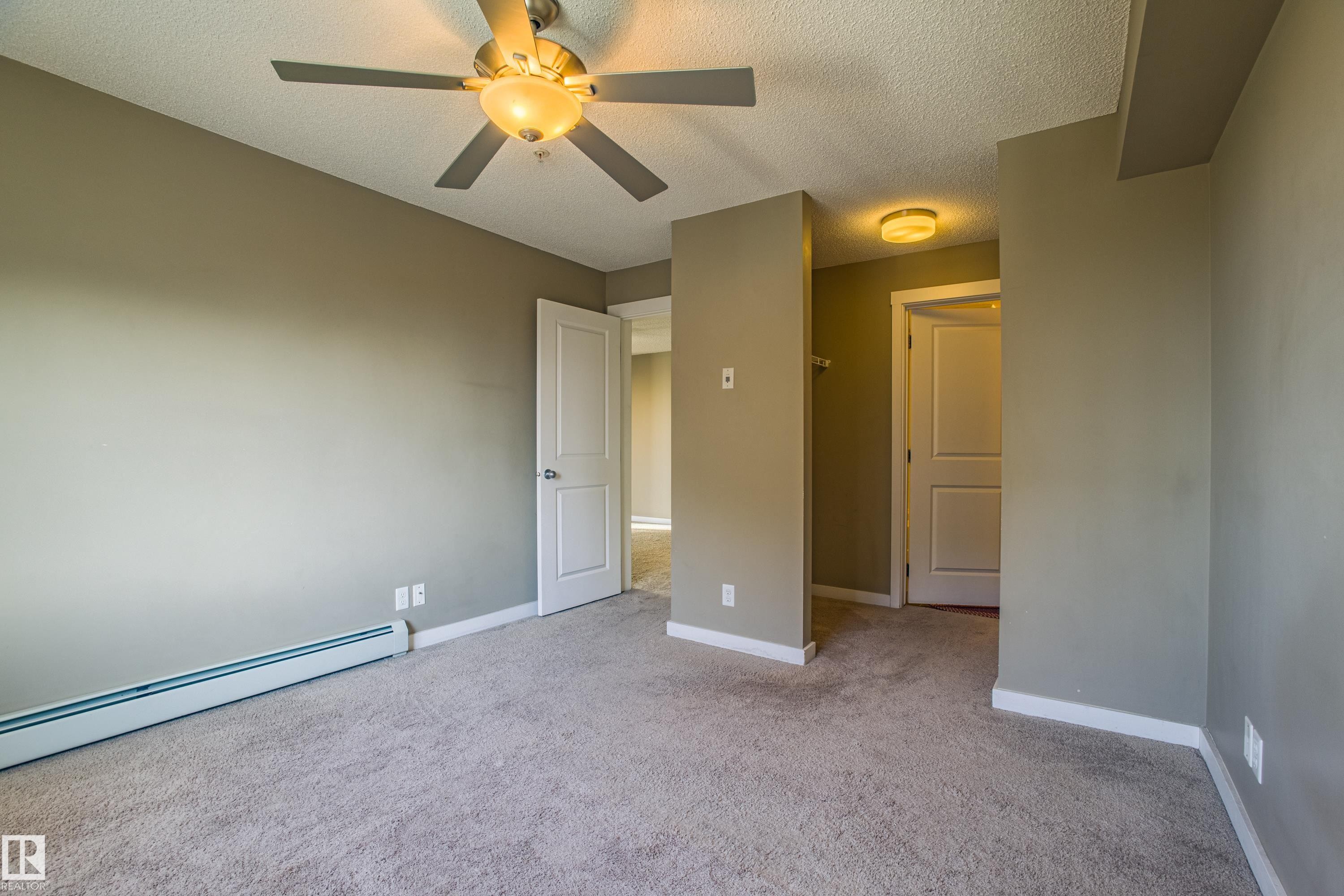 Unfurnished bedroom featuring a textured ceiling, light colored carpet, a ceiling fan, and baseboard heating - 201 5804 Mullen Place, Edmonton, AB - Indoor Photo Showing Other Room