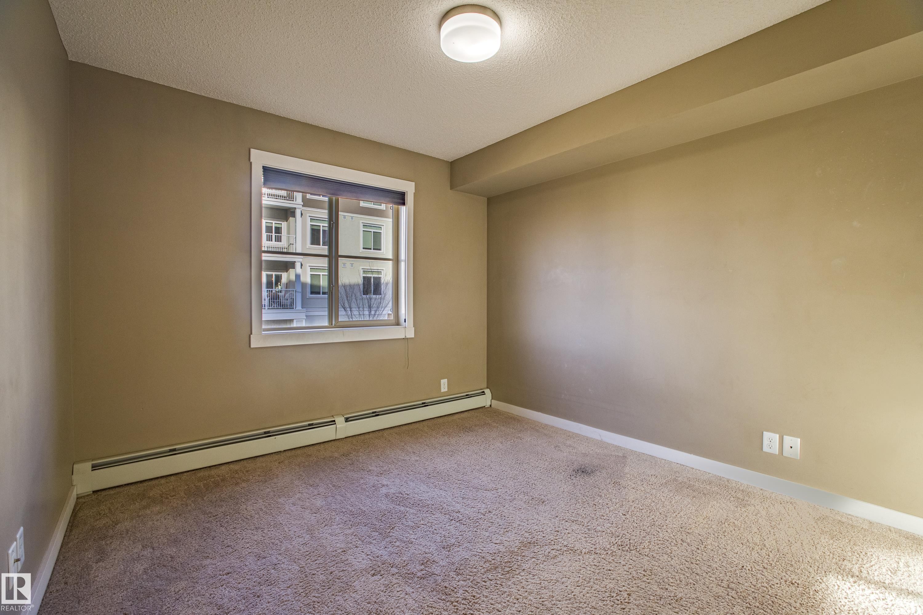 Carpeted spare room featuring a textured ceiling and baseboard heating - 201 5804 Mullen Place, Edmonton, AB - Indoor Photo Showing Other Room