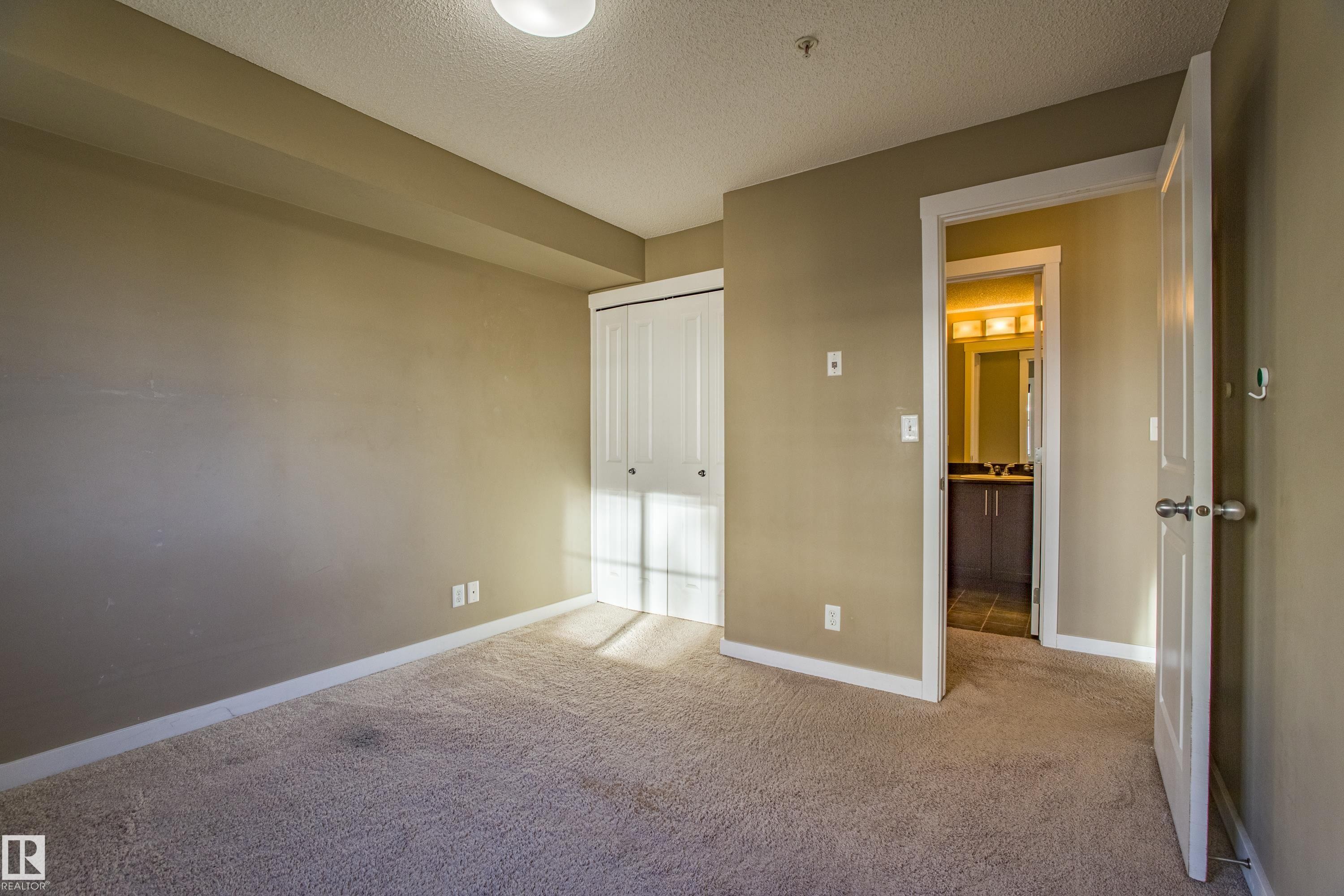 Unfurnished bedroom featuring a textured ceiling, carpet flooring, and a closet - 201 5804 Mullen Place, Edmonton, AB - Indoor Photo Showing Other Room