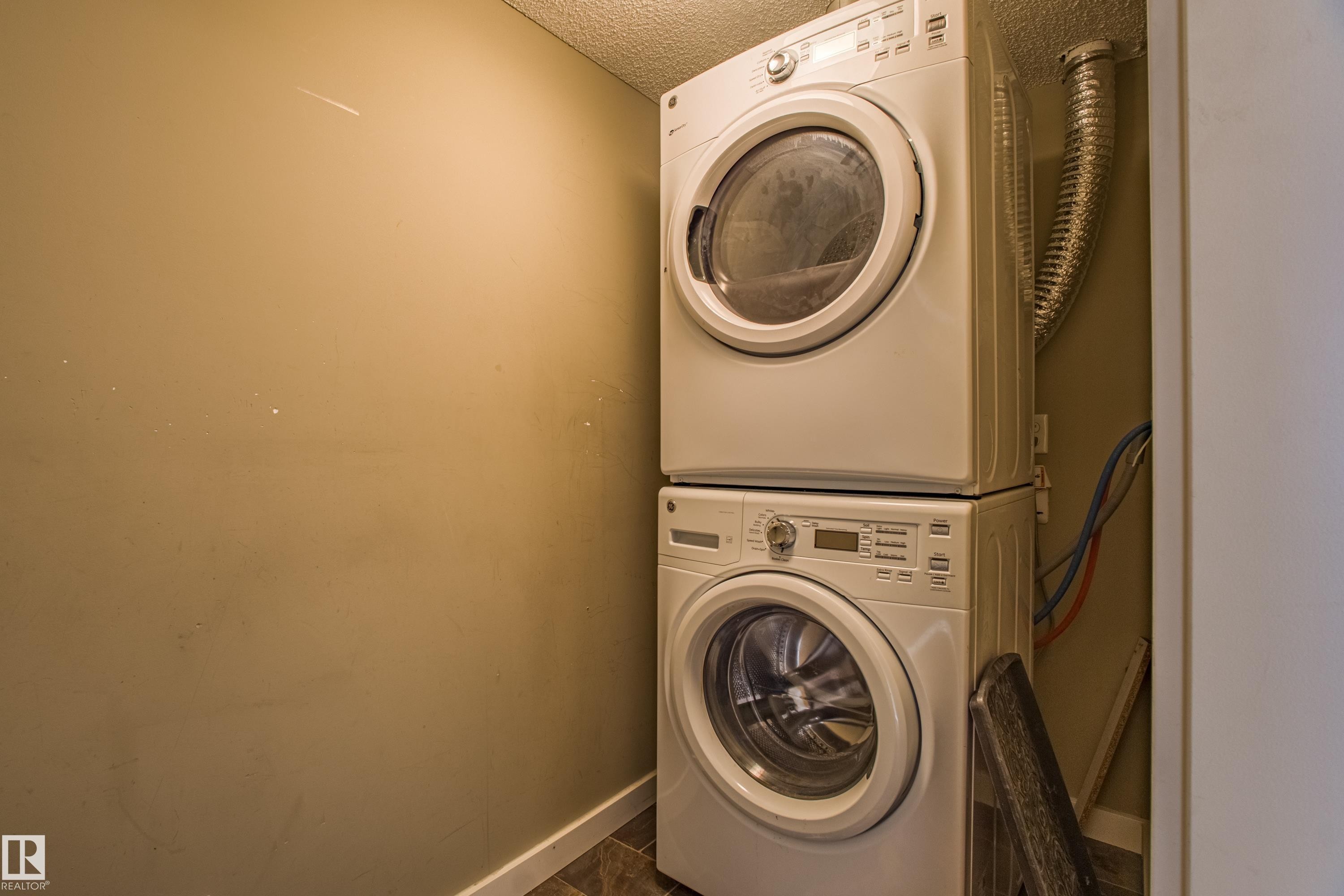 Laundry area featuring stacked washer / drying machine and a textured ceiling - 201 5804 Mullen Place, Edmonton, AB - Indoor Photo Showing Laundry Room