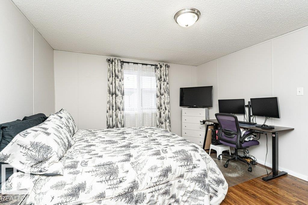 Bedroom with dark wood-style floors, a textured ceiling, a decorative wall, and an office area - 1637 68 Avenue, Edmonton, AB - Indoor Photo Showing Bedroom
