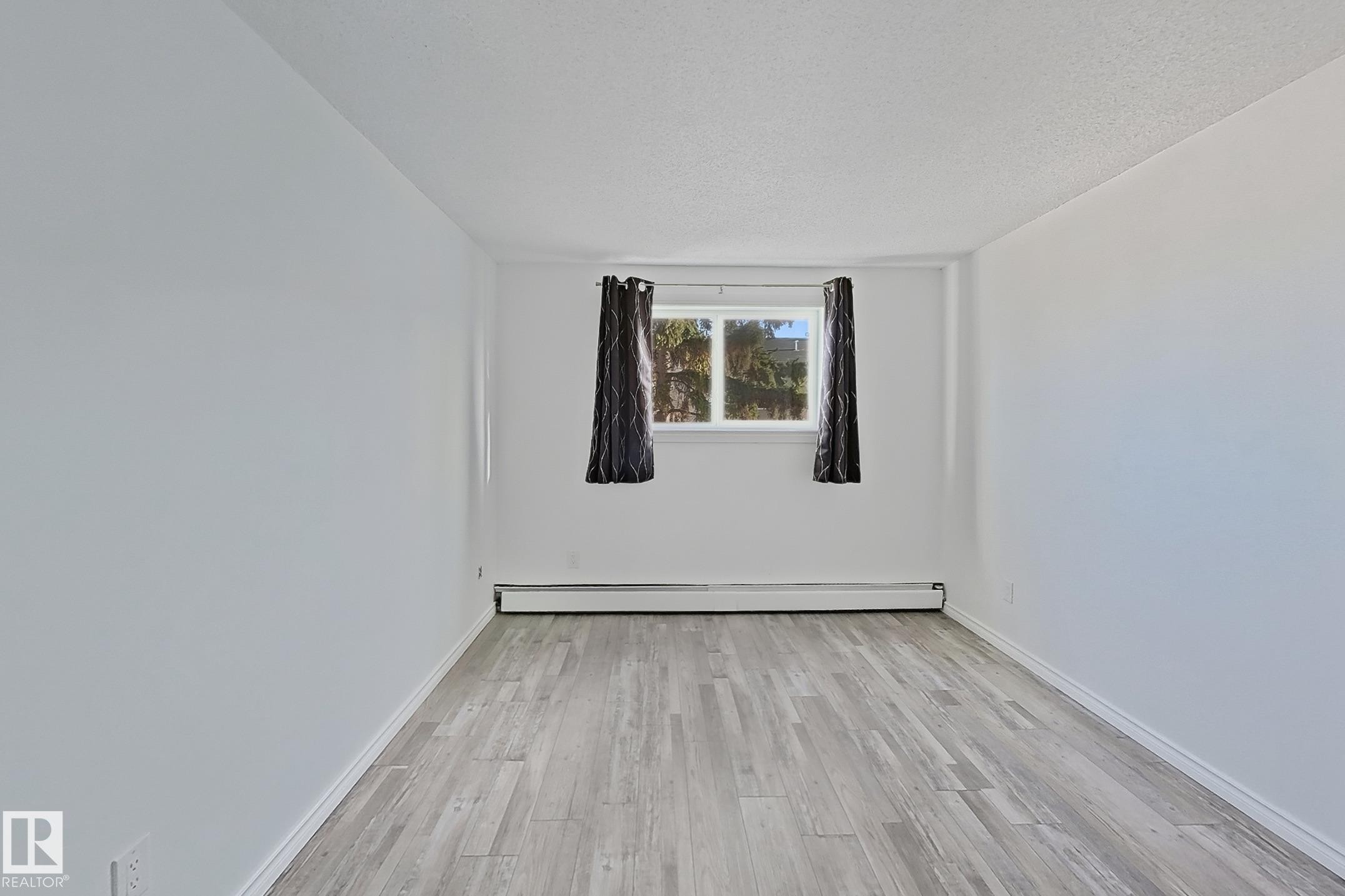 Spare room featuring light wood-type flooring, baseboard heating, and a textured ceiling - 309 1624 48 Street, Edmonton, AB - Indoor Photo Showing Other Room