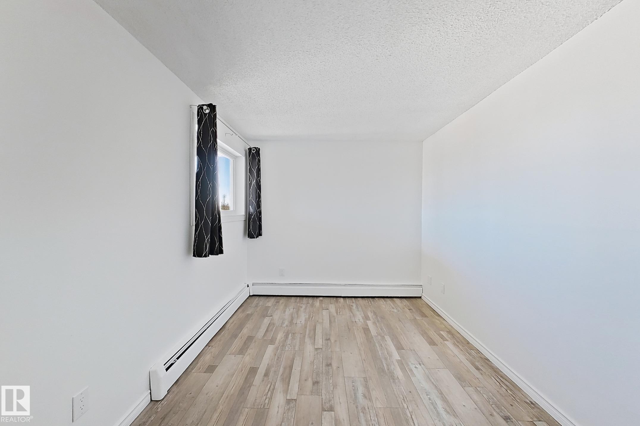 Unfurnished room with baseboard heating, a textured ceiling, and light wood-style floors - 309 1624 48 Street, Edmonton, AB - Indoor Photo Showing Other Room
