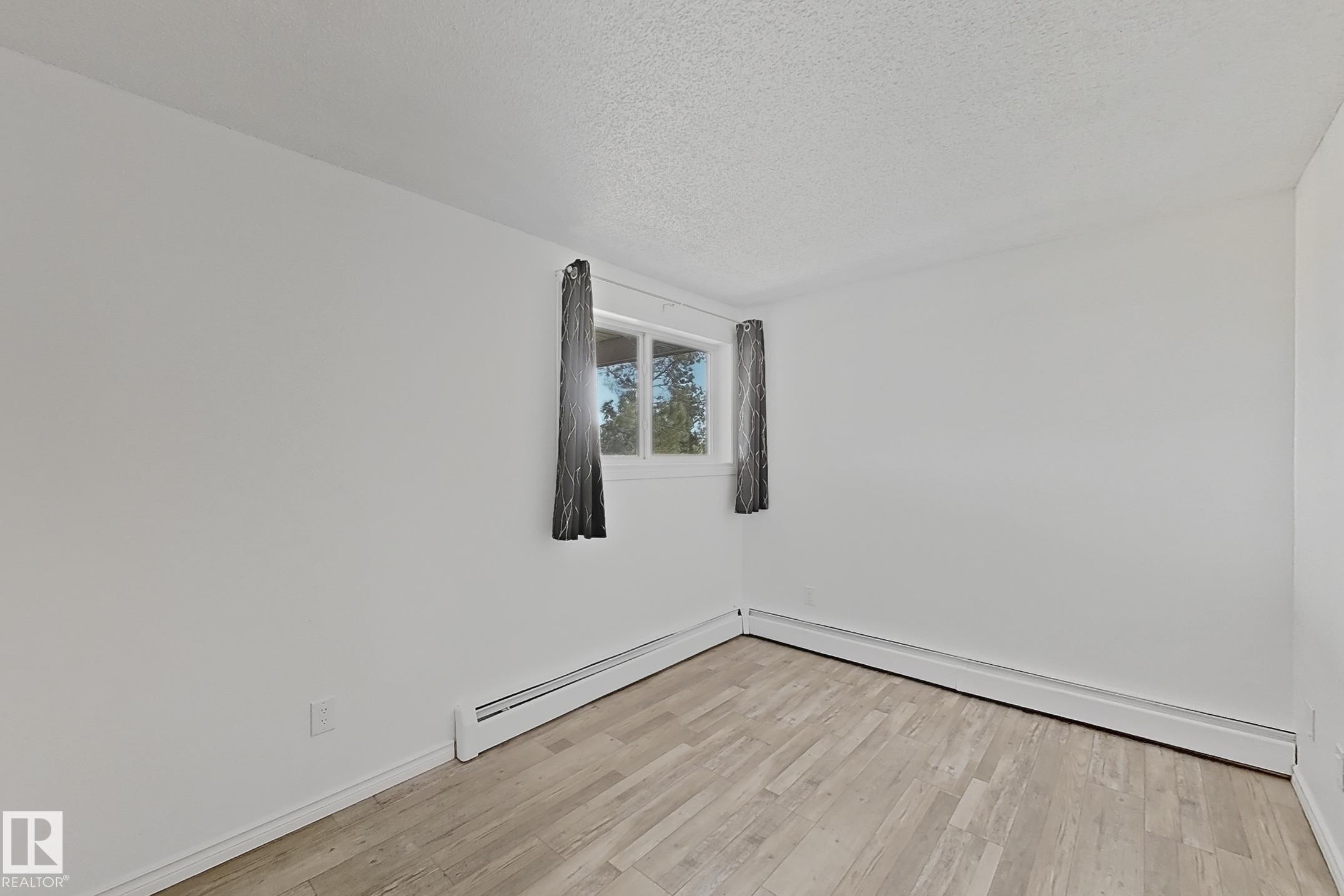 Spare room featuring light wood finished floors, a textured ceiling, and a baseboard heating unit - 309 1624 48 Street, Edmonton, AB - Indoor Photo Showing Other Room