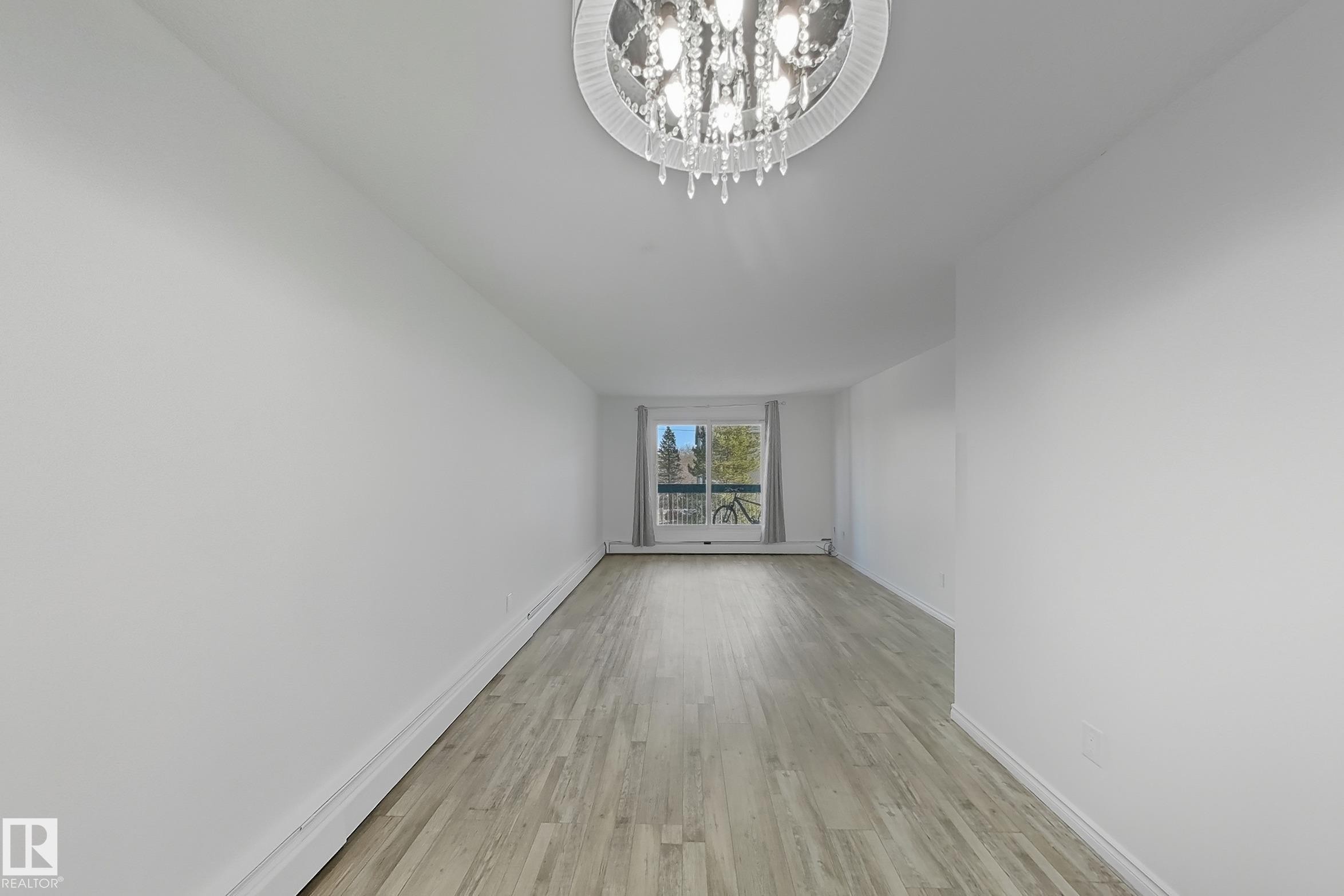 Unfurnished living room featuring light wood-type flooring, a baseboard radiator, and a chandelier - 309 1624 48 Street, Edmonton, AB - Indoor Photo Showing Other Room