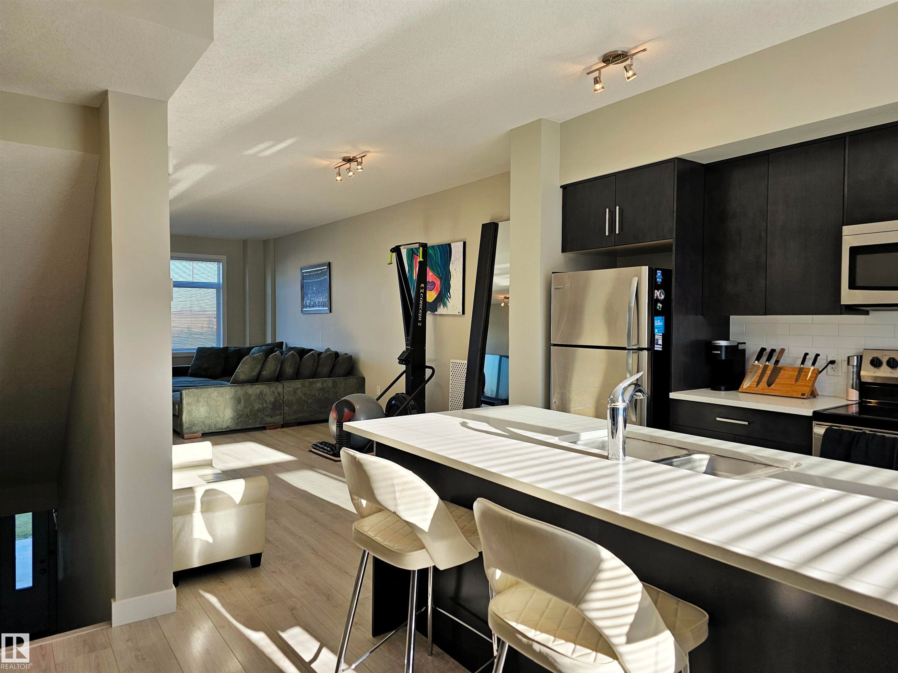 Kitchen featuring dark cabinetry, stainless steel appliances, light wood finished floors, a breakfast bar, and open floor plan - 83 600 Bellerose Drive, St. Albert, AB - Indoor Photo Showing Kitchen With Stainless Steel Kitchen With Double Sink