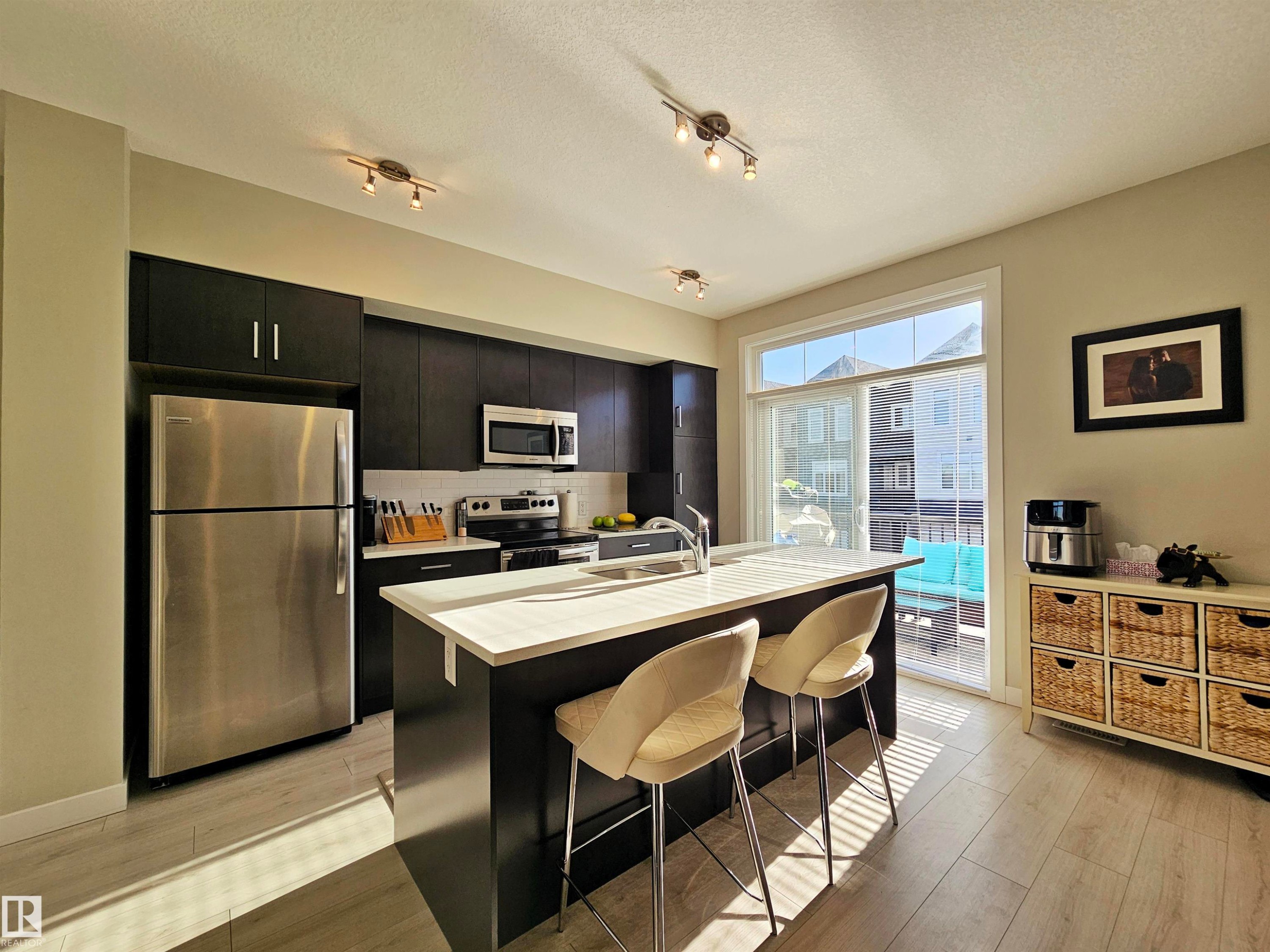 Kitchen featuring dark cabinetry, appliances with stainless steel finishes, light countertops, tasteful backsplash, and a center island with sink - 83 600 Bellerose Drive, St. Albert, AB - Indoor Photo Showing Kitchen With Stainless Steel Kitchen