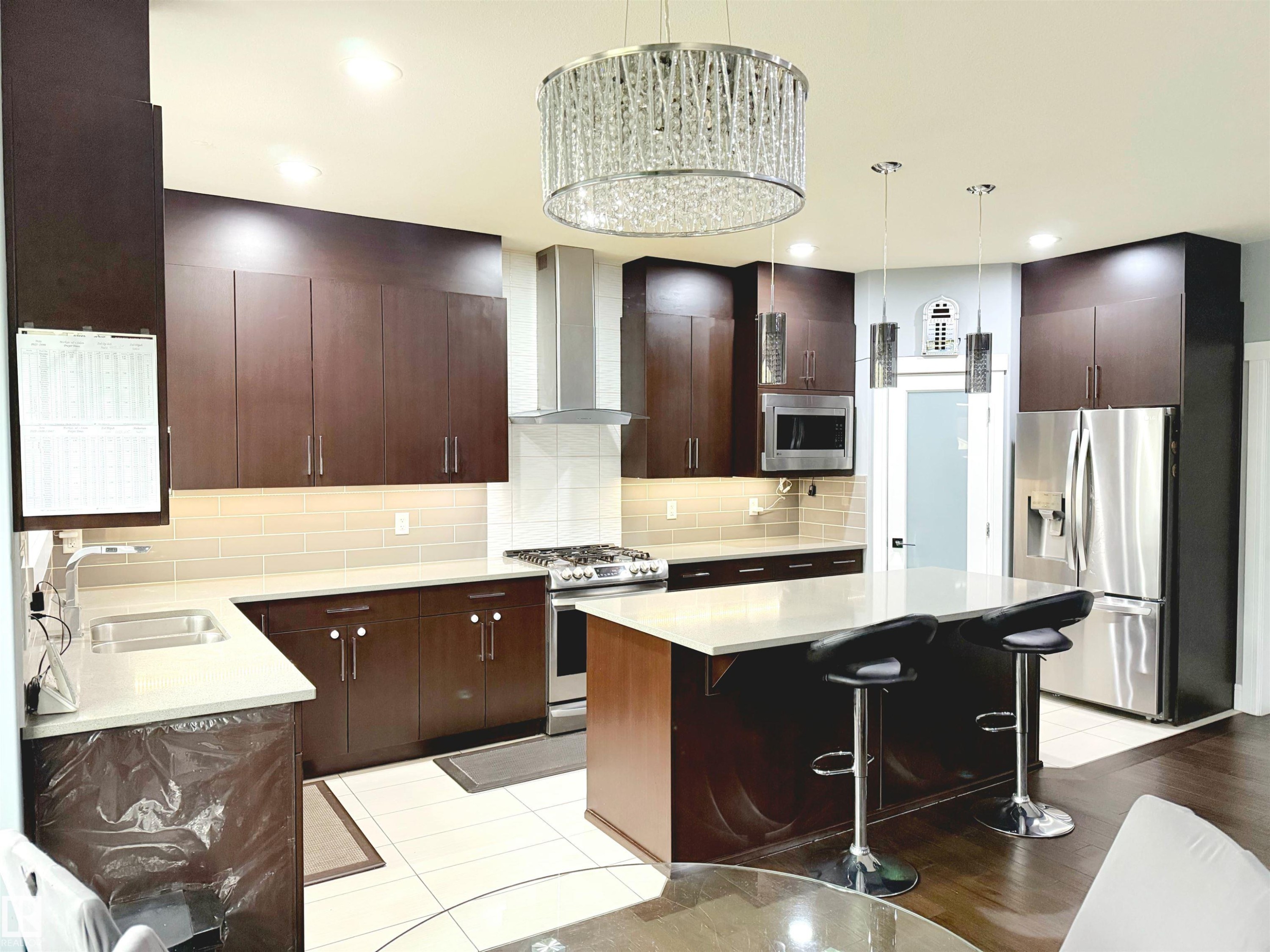 Kitchen with a kitchen bar, stainless steel appliances, wall chimney range hood, backsplash, and a kitchen island - 1357 Watt Drive, Edmonton, AB - Indoor Photo Showing Kitchen With Stainless Steel Kitchen With Double Sink With Upgraded Kitchen