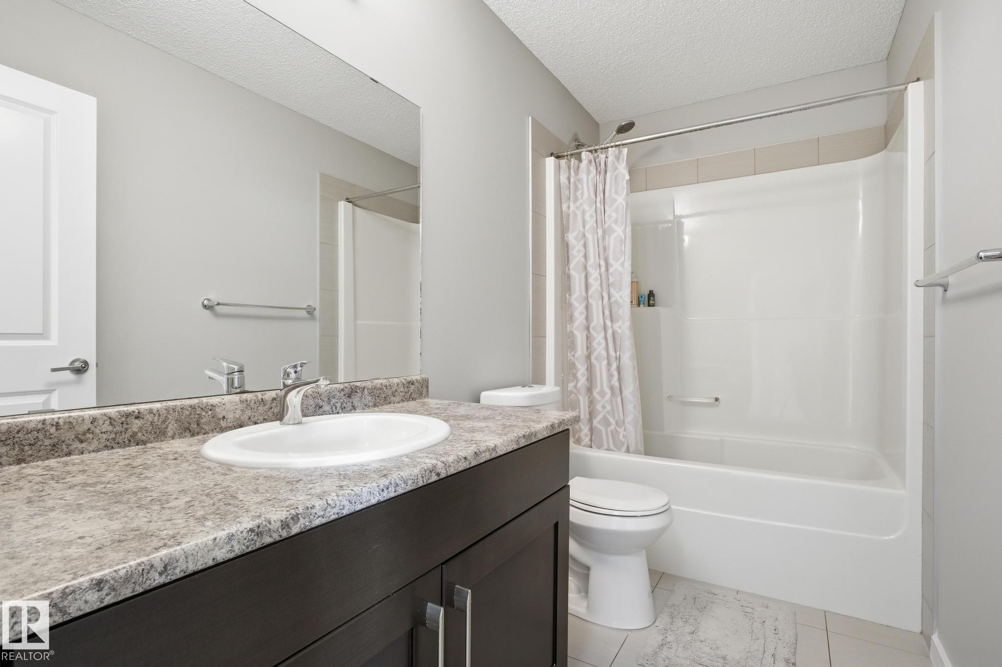 Full bath featuring a textured ceiling, vanity, light tile patterned floors, and shower / tub combo - 893 Ebbers Crescent Nw, Edmonton, AB - Indoor Photo Showing Bathroom
