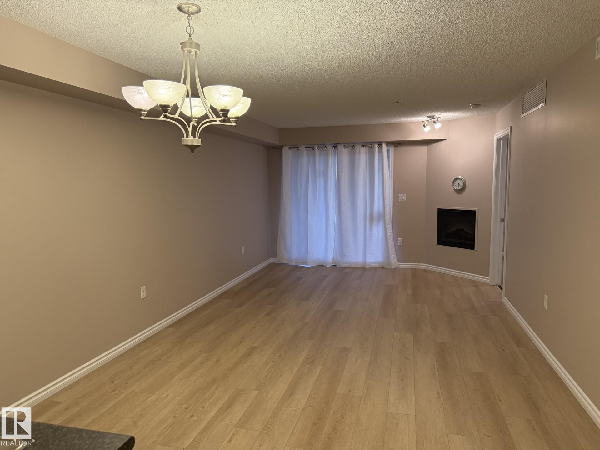 Unfurnished dining area featuring a textured ceiling, a chandelier, light wood finished floors, and a fireplace - 303 10118 106 Avenue, Edmonton, AB - Indoor Photo Showing Other Room