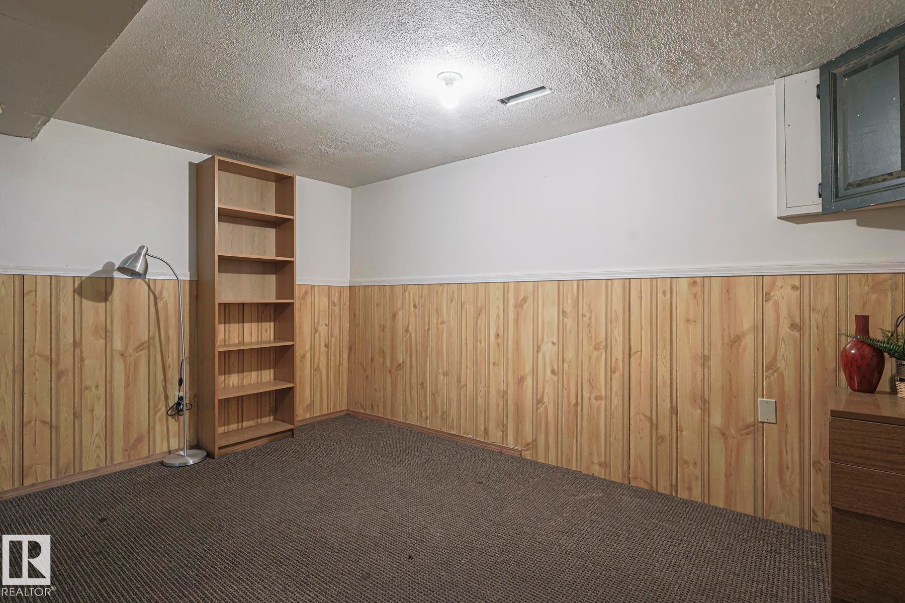 Empty room featuring wood walls, a textured ceiling, wainscoting, and dark carpet - 51 Belmead Gardens, Edmonton, AB - Indoor Photo Showing Other Room