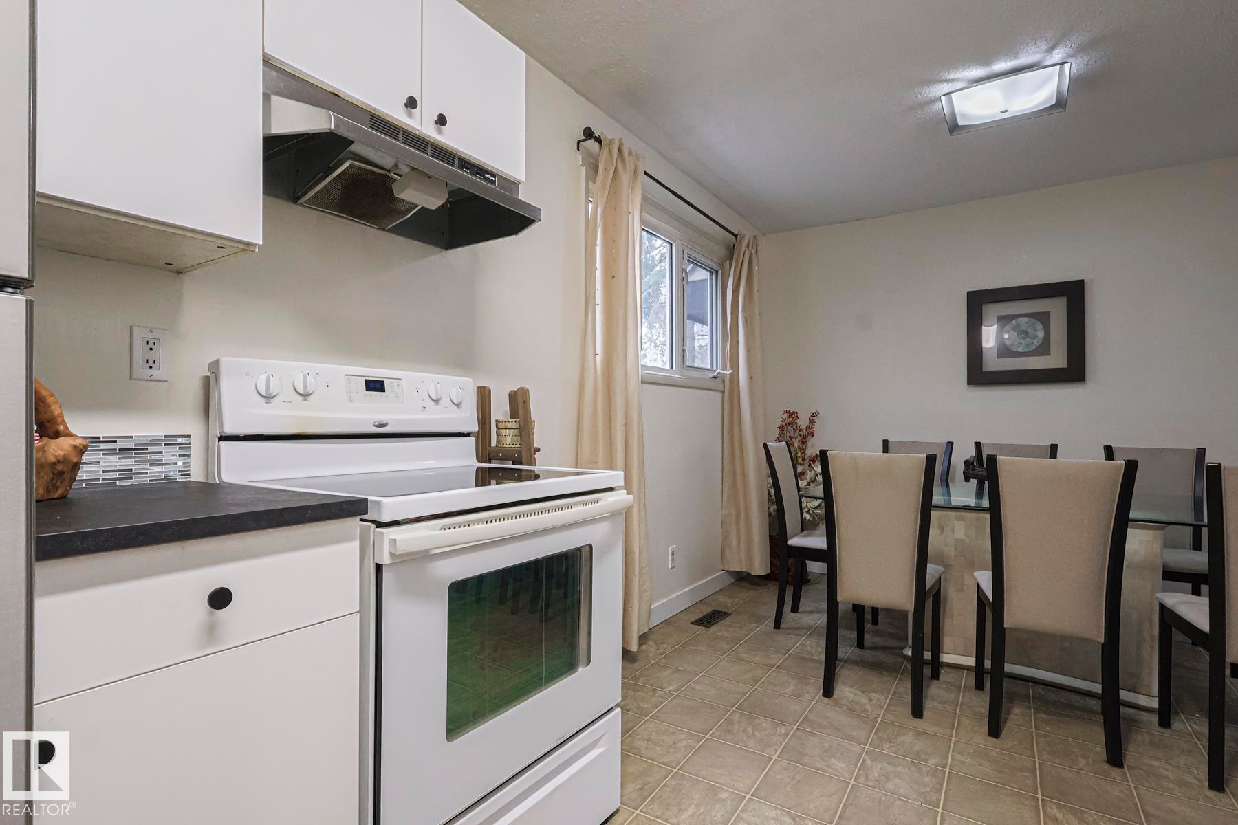 Kitchen with electric stove, white cabinetry, under cabinet range hood, dark countertops, and light tile patterned floors - 51 Belmead Gardens, Edmonton, AB - Indoor Photo Showing Kitchen